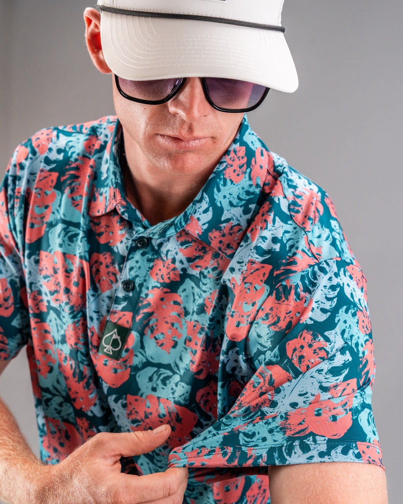 A golfer models a vibrant teal shirt featuring a painted monstera leaf pattern, showcasing bold colors and style.