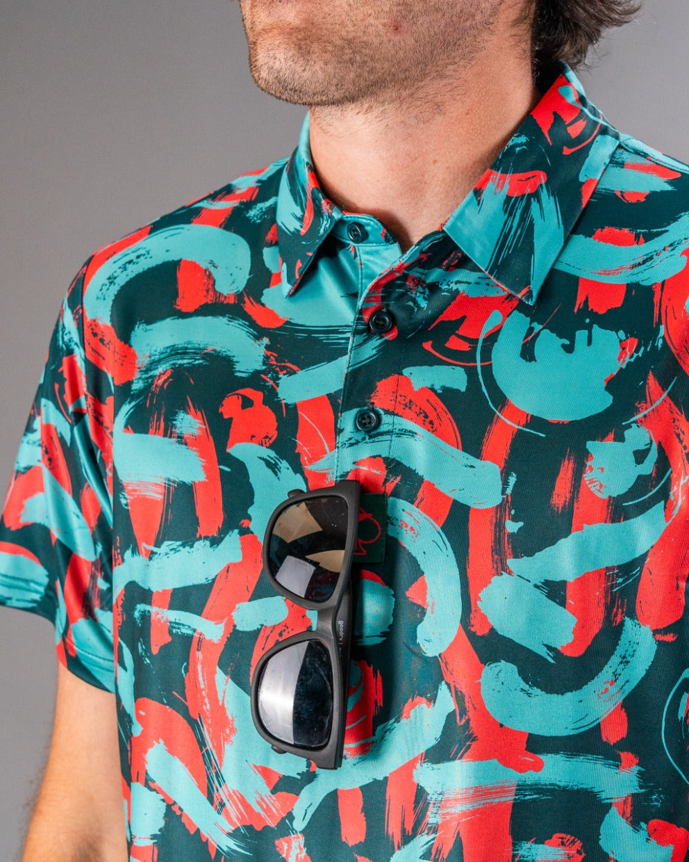 Bold golf shirt featuring a vibrant paint strokes pattern in coral, teal, and black, perfect for stylish golfers.