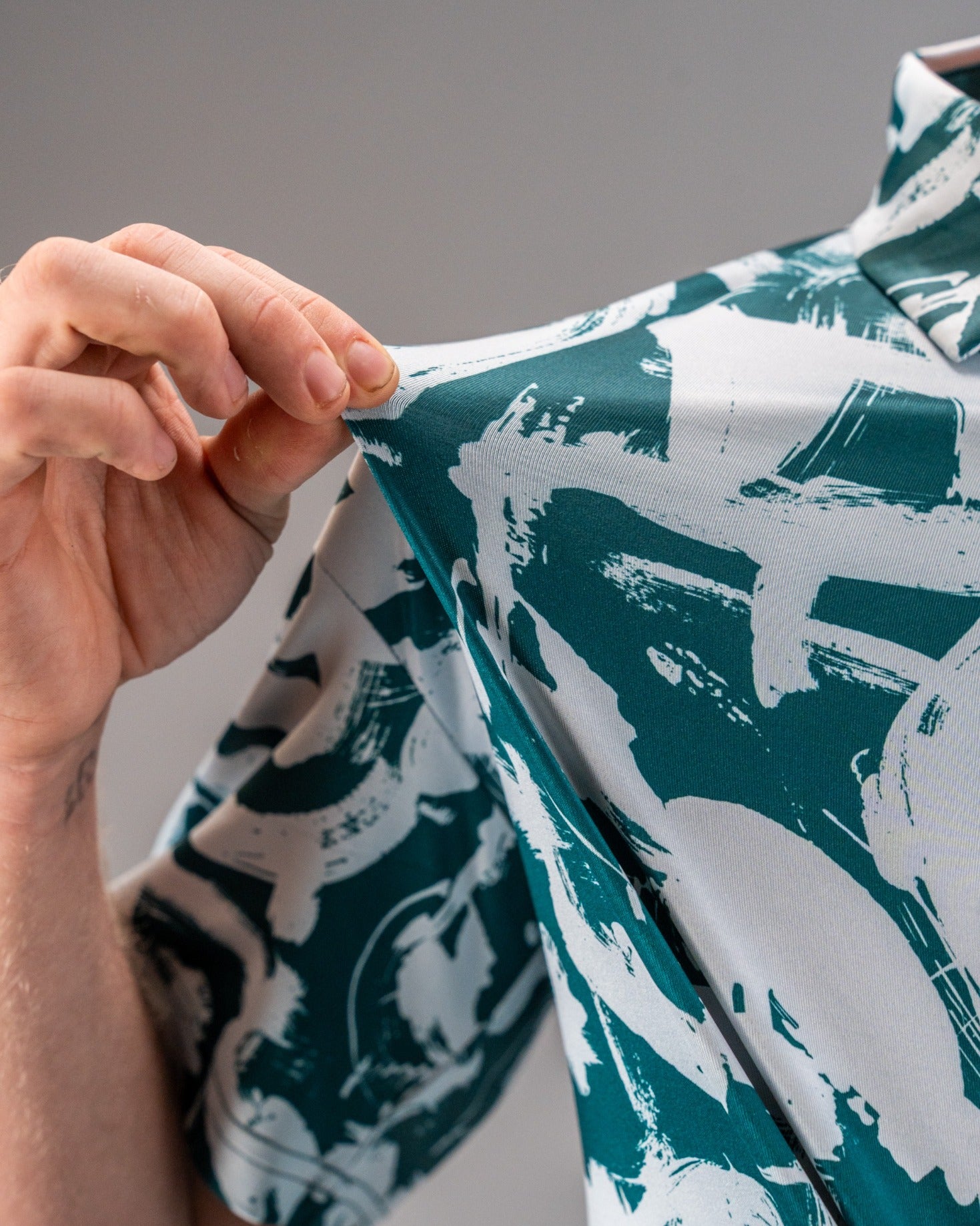 Close-up of a golfer adjusting the collar of a Paint Strokes Green shirt featuring a bold, abstract brushstroke design.