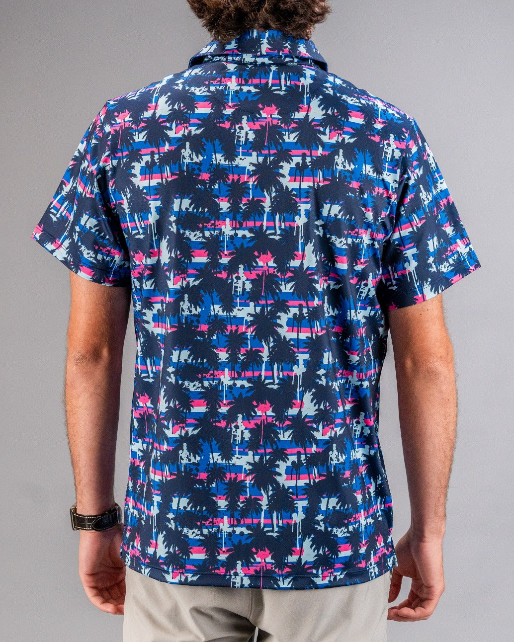 Men's short-sleeve golf shirt featuring a vibrant palm tree pattern in blue, pink, and white against a dark background.