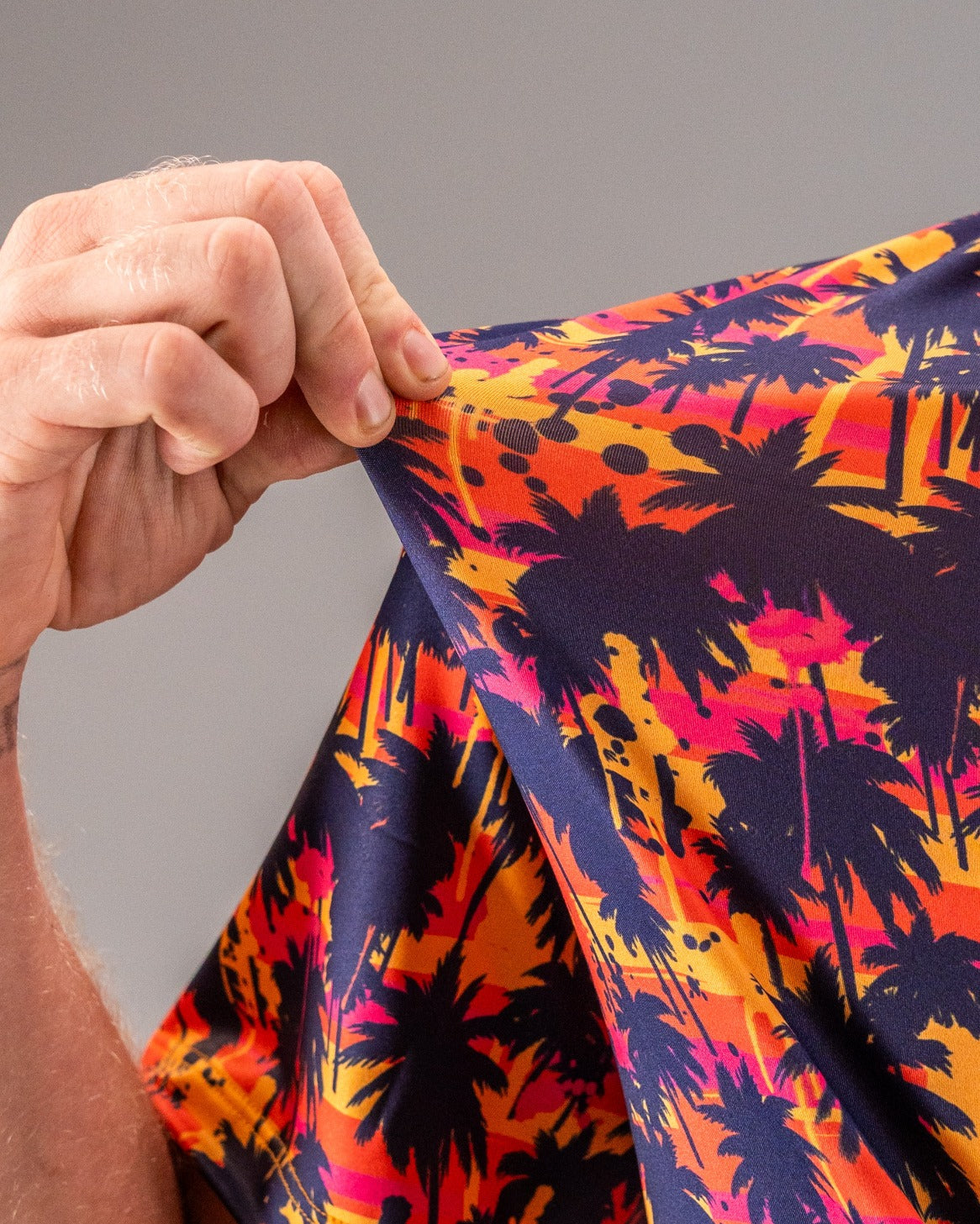 Close-up of vibrant tropical palm tree print in pink, orange, and navy on bold golf apparel fabric.