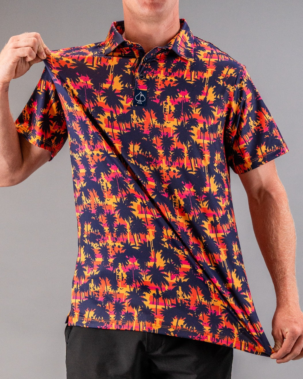 Bright, tropical-themed golf polo with a sunset palm tree print in orange, pink, and navy, designed for bold, standout style.