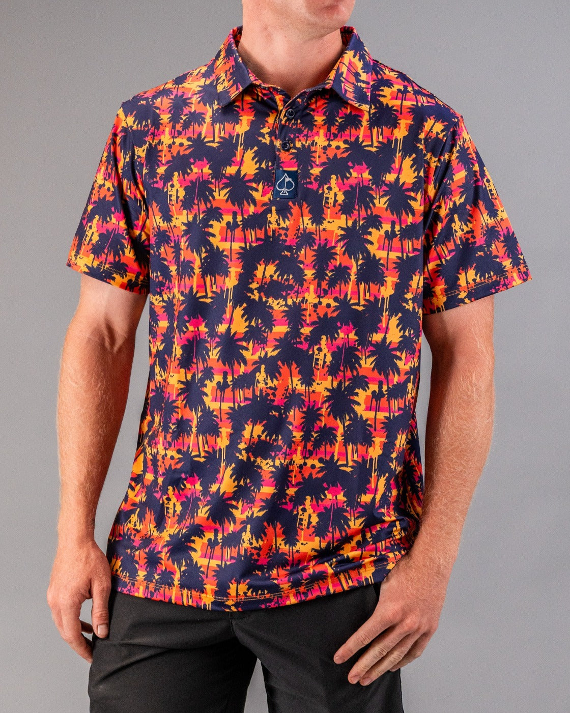 Bold golf polo featuring a vibrant palm tree pattern in shades of orange, pink, and purple against a dark background.