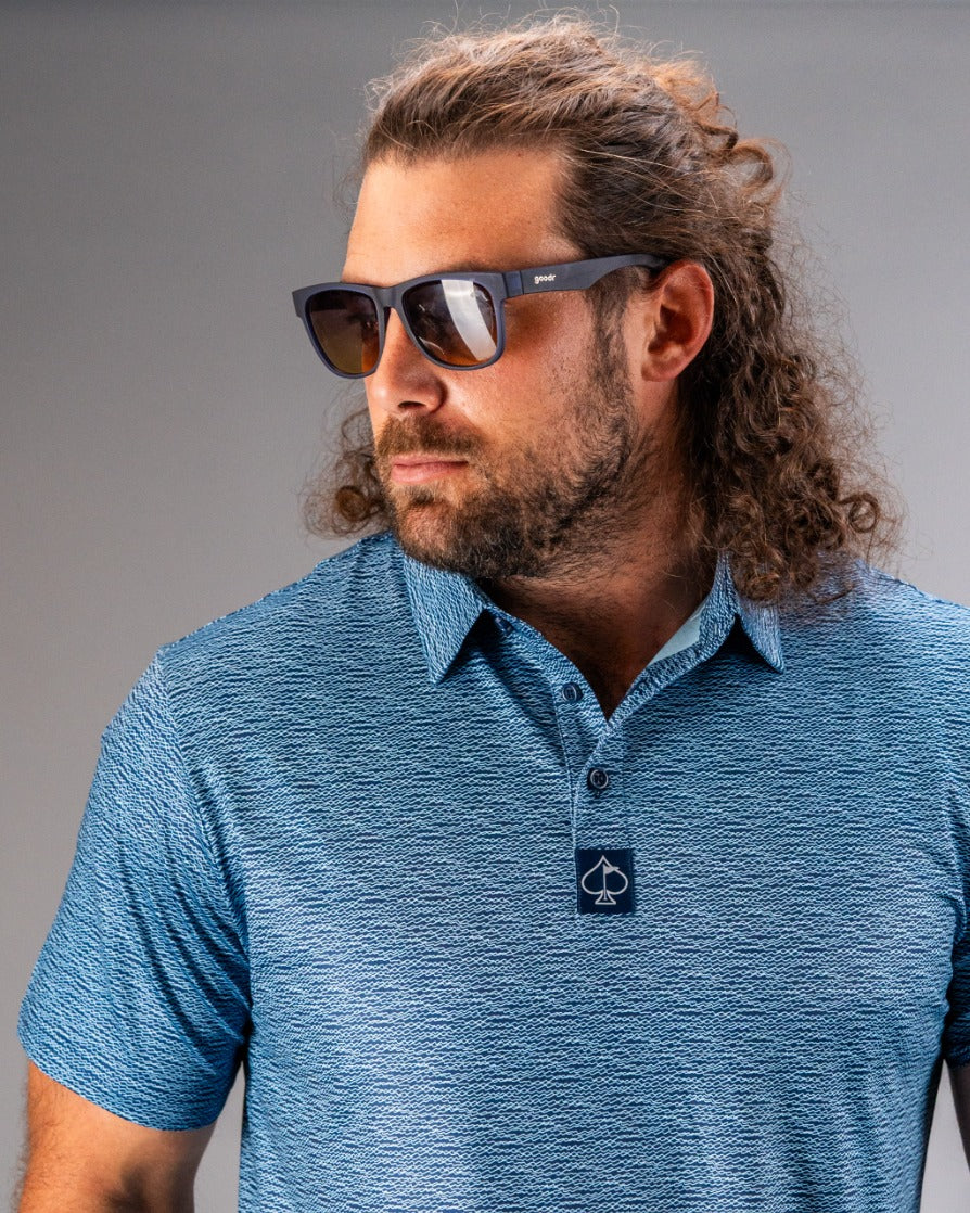 Man wearing a blue patterned golf polo shirt with a collar, showcasing a stylish look with sunglasses.
