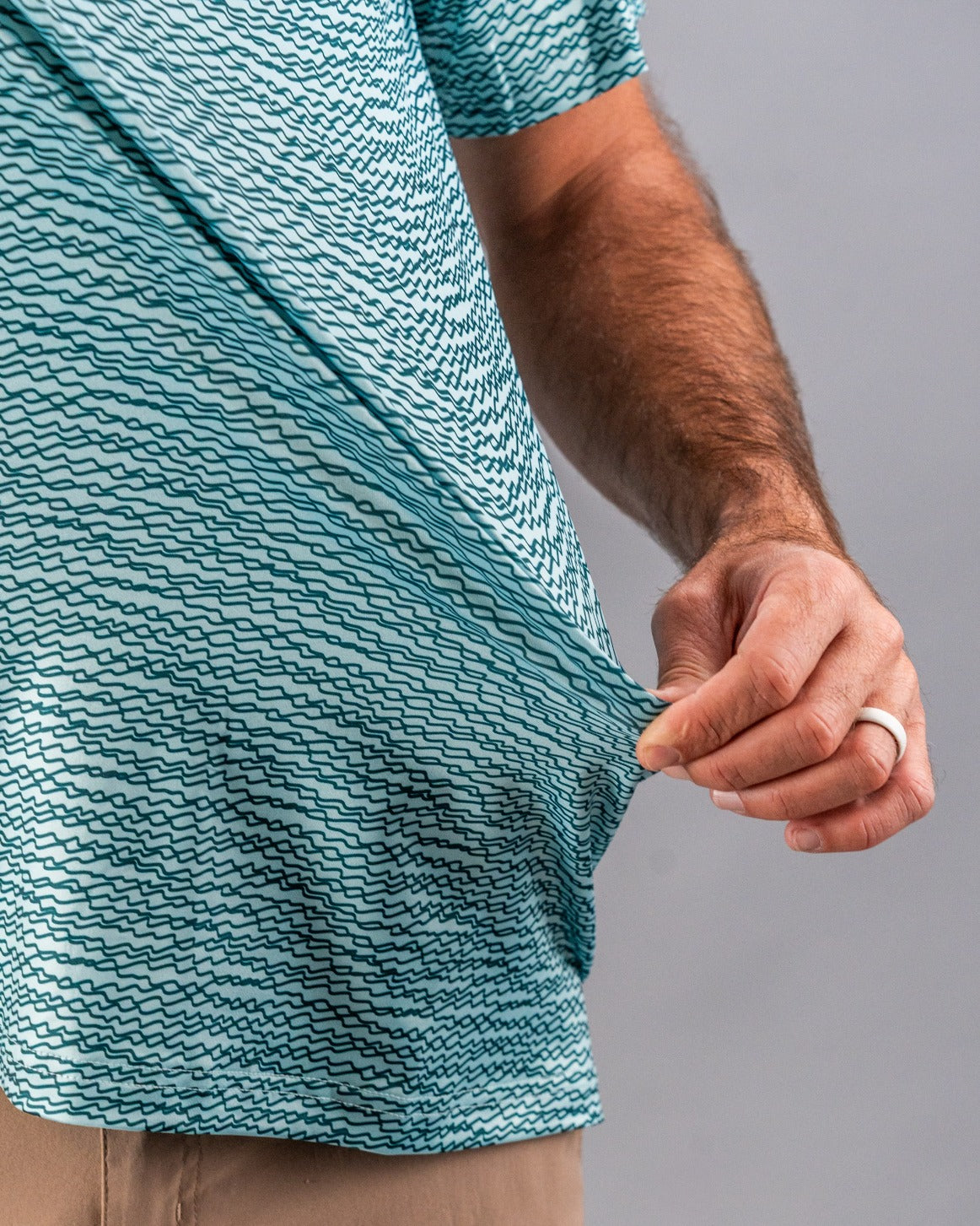 Teal golf shirt with a squiggle pattern, showcasing a close-up of the fabric being pulled by a hand.