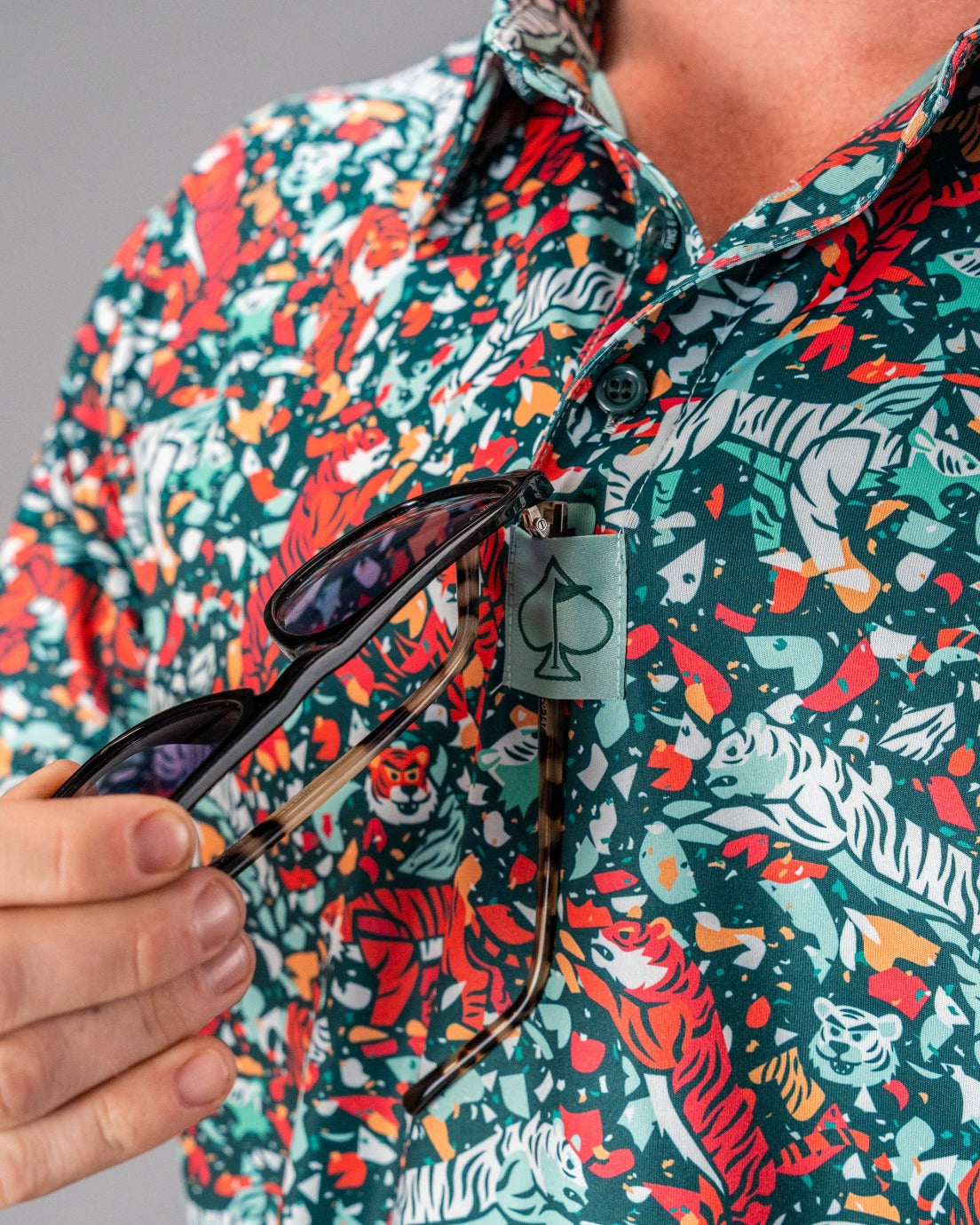 Bold teal golf shirt featuring a vibrant tiger print, with sunglasses hanging from a stylish tag. Perfect for standout golfers.