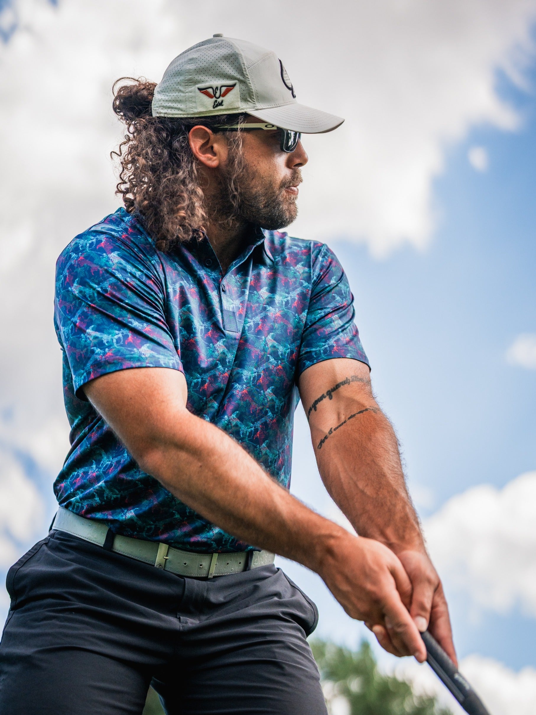 Bold golf polo featuring a vibrant swordfish pattern, worn by a golfer preparing to swing under a blue sky.