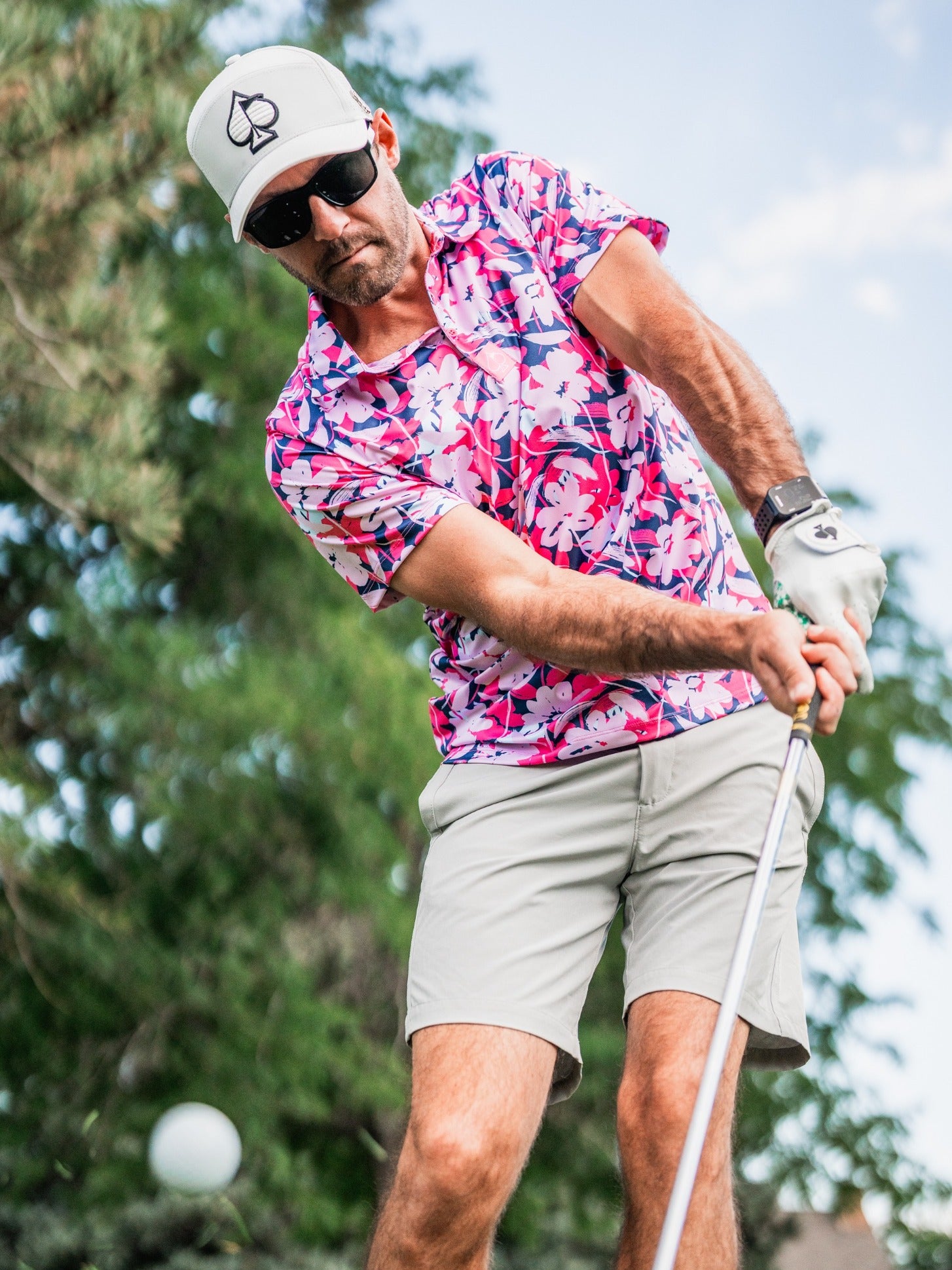 A golfer in a vibrant floral polo shirt and cap swings a club on the course, showcasing bold golf style.