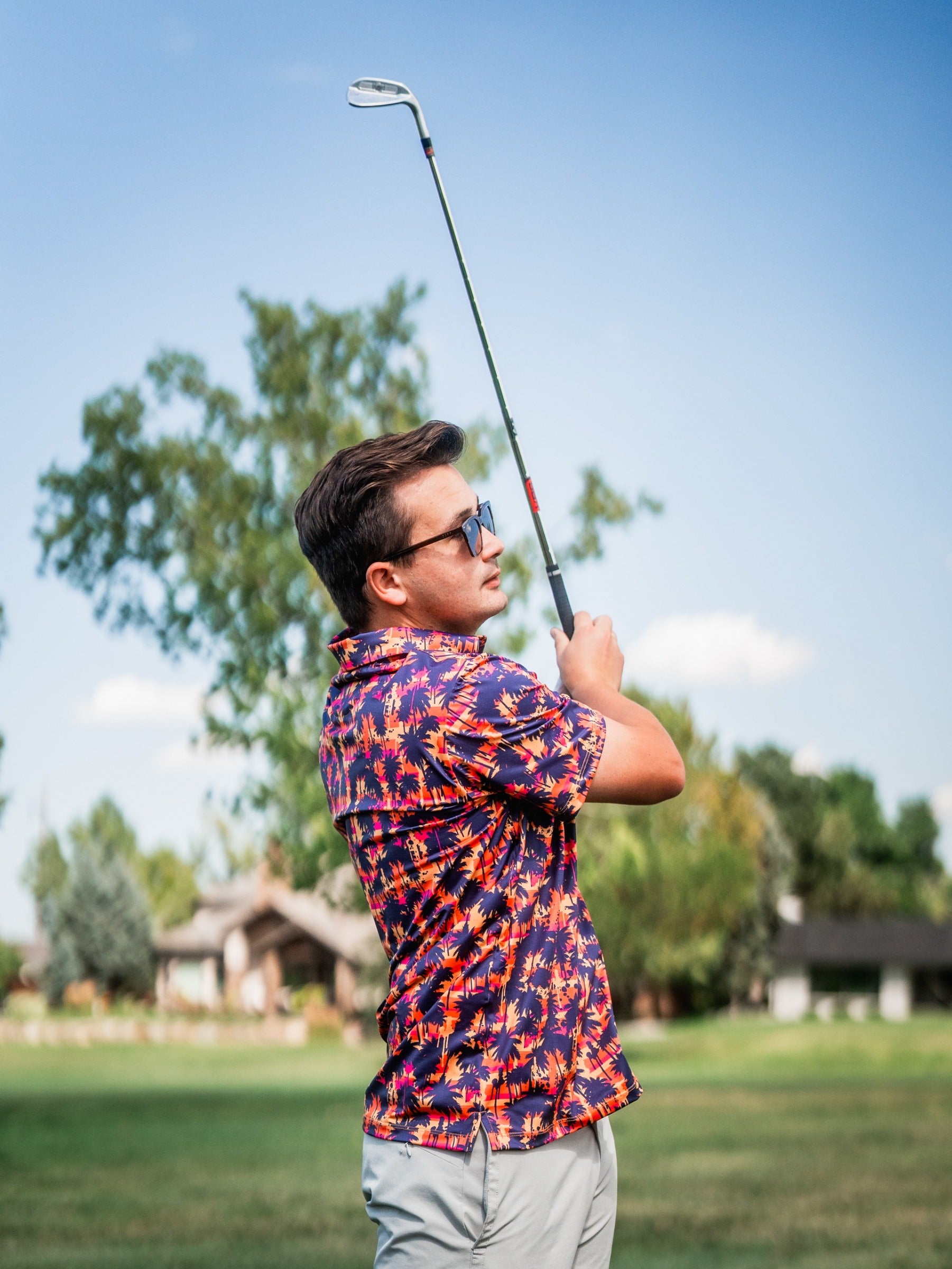 A golfer swings a club while wearing a vibrant palm-patterned shirt, showcasing bold style on the course.