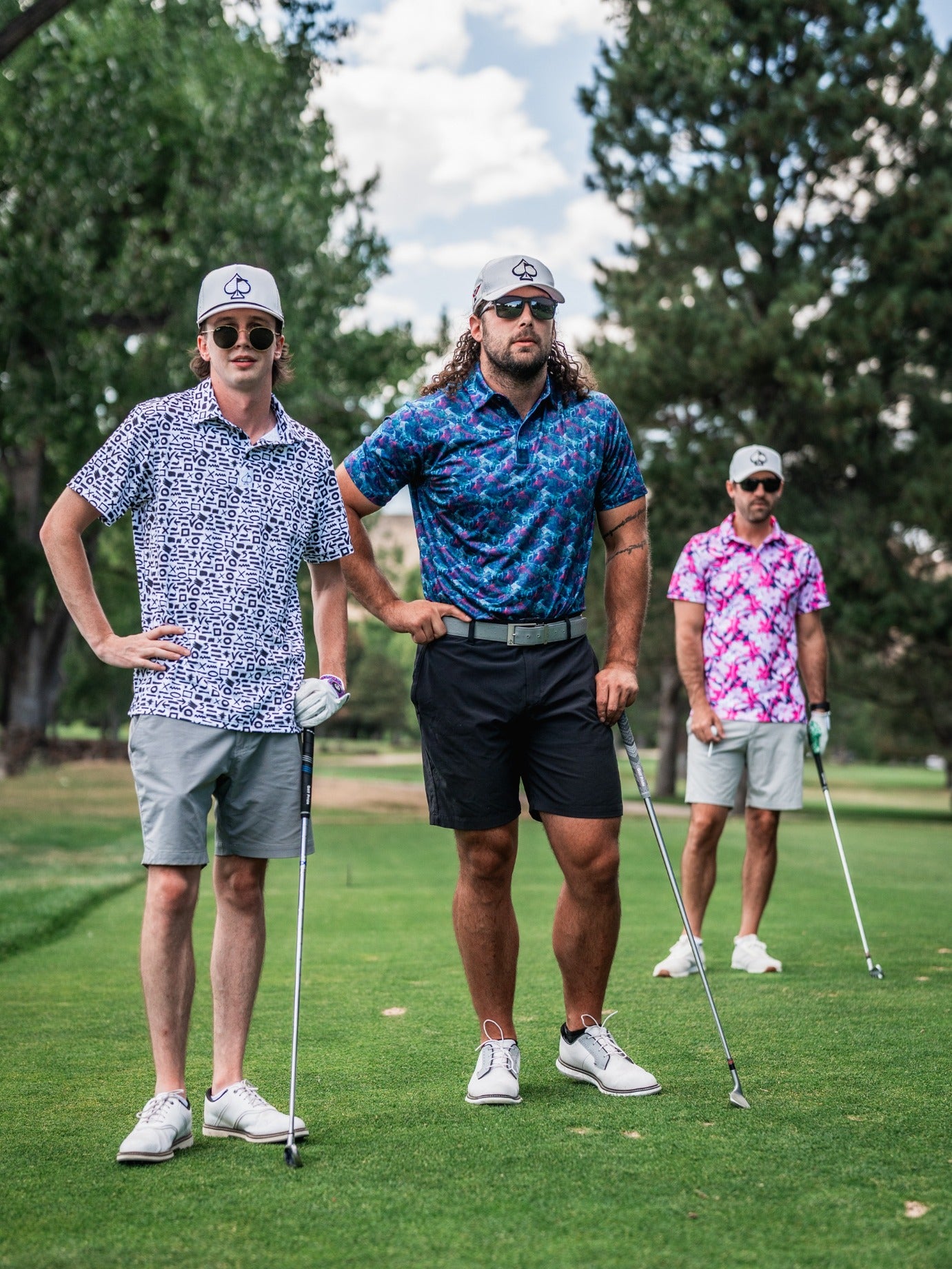 Three golfers in colorful, bold patterned shirts, wearing stylish caps and sunglasses, standing on a lush golf course.