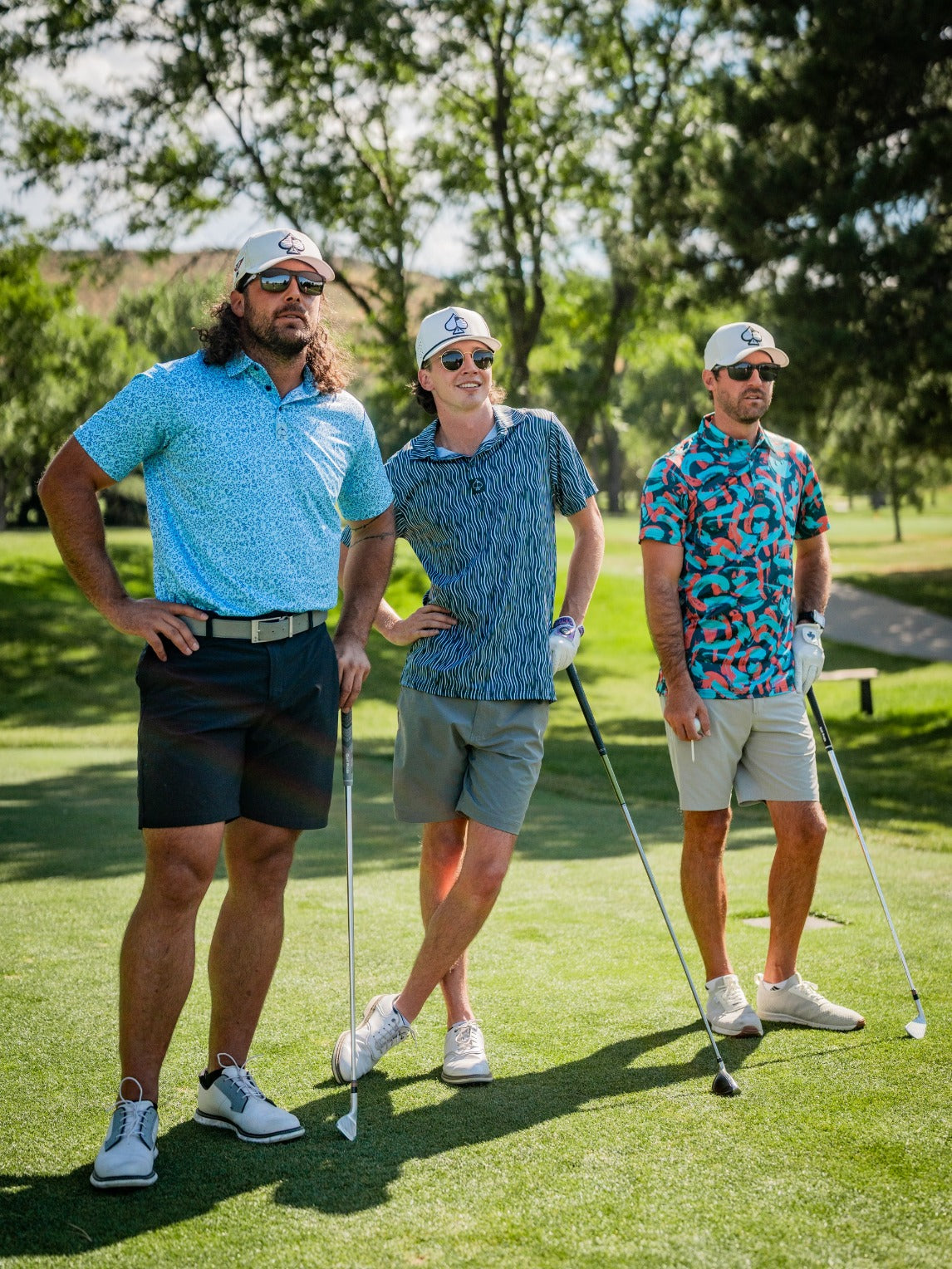 Group of three golfers in colorful, bold golf apparel with unique headcovers, standing on lush green course in sunlight.