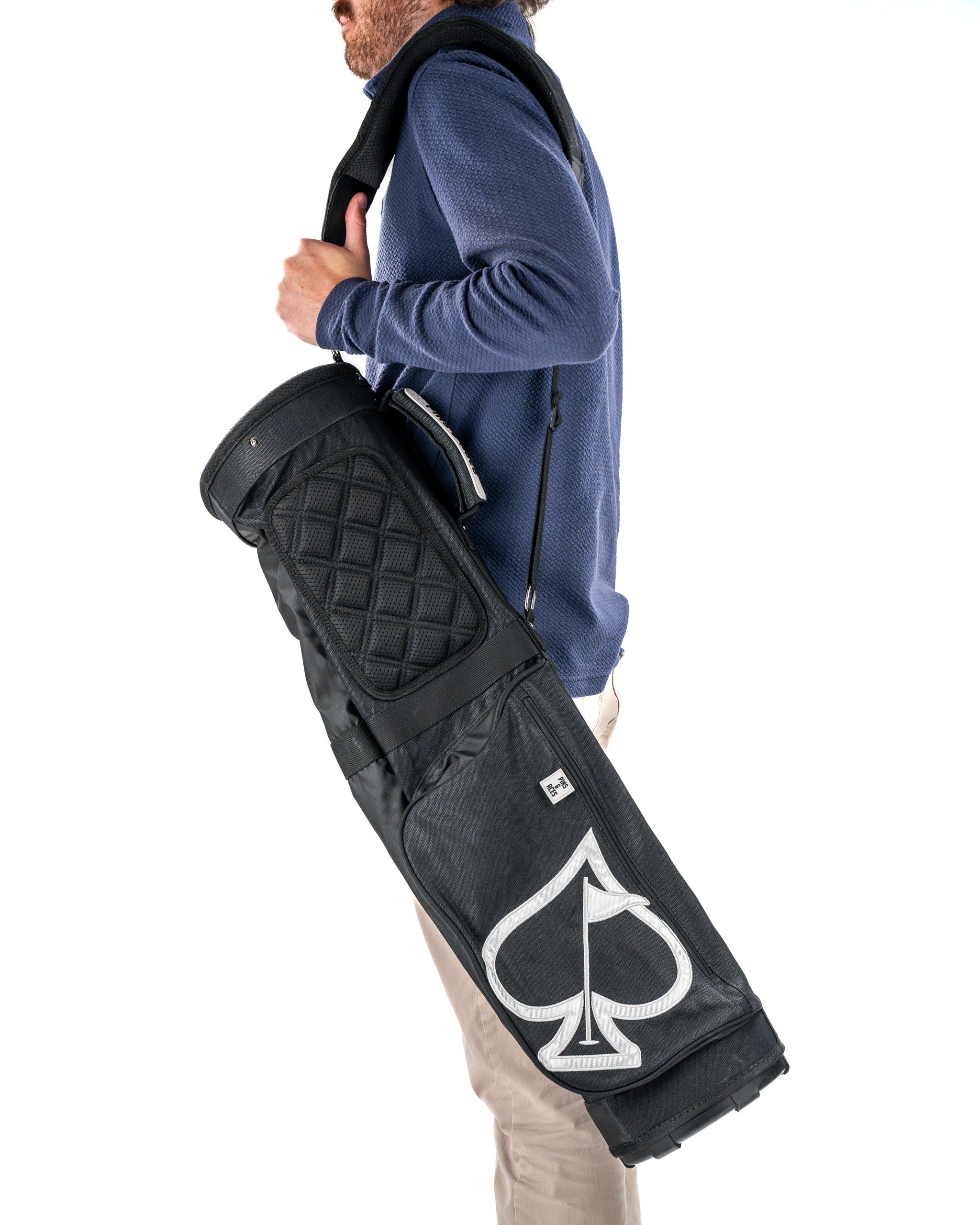 A golfer carrying a sleek black Sunday golf bag featuring a white spade logo, showcasing its stylish design and functionality.
