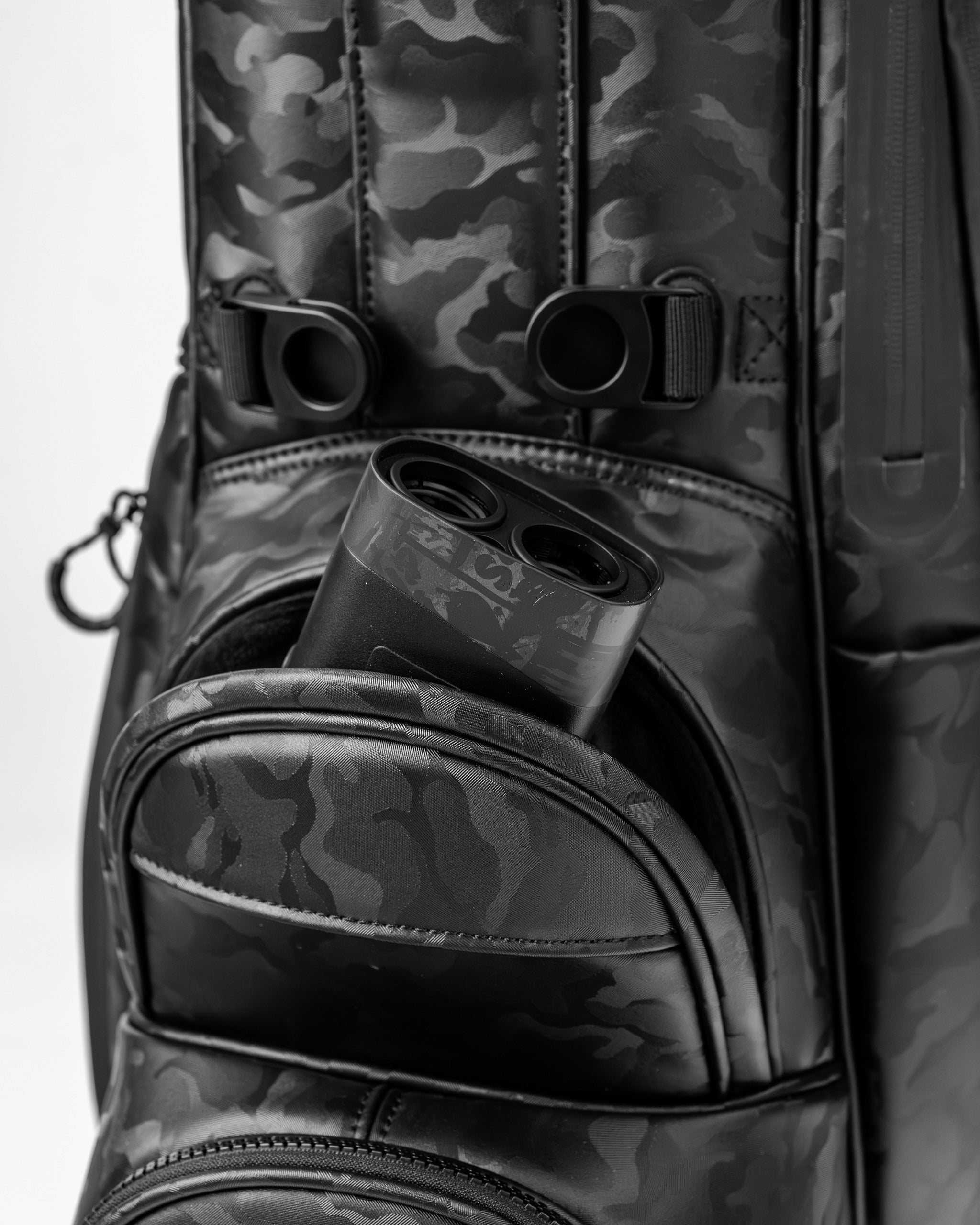 Black camo golf bag featuring a pocket with a golf rangefinder partially visible, showcasing its sleek design.