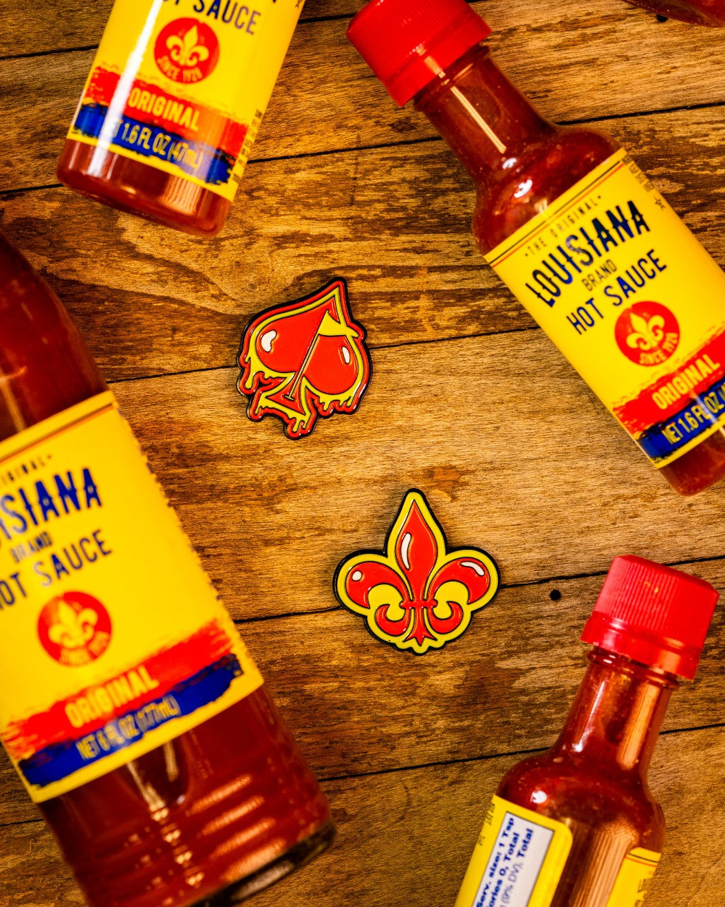 Fleur-de-lis ball marker surrounded by Louisiana hot sauce bottles on a wooden surface, showcasing vibrant colors and design.