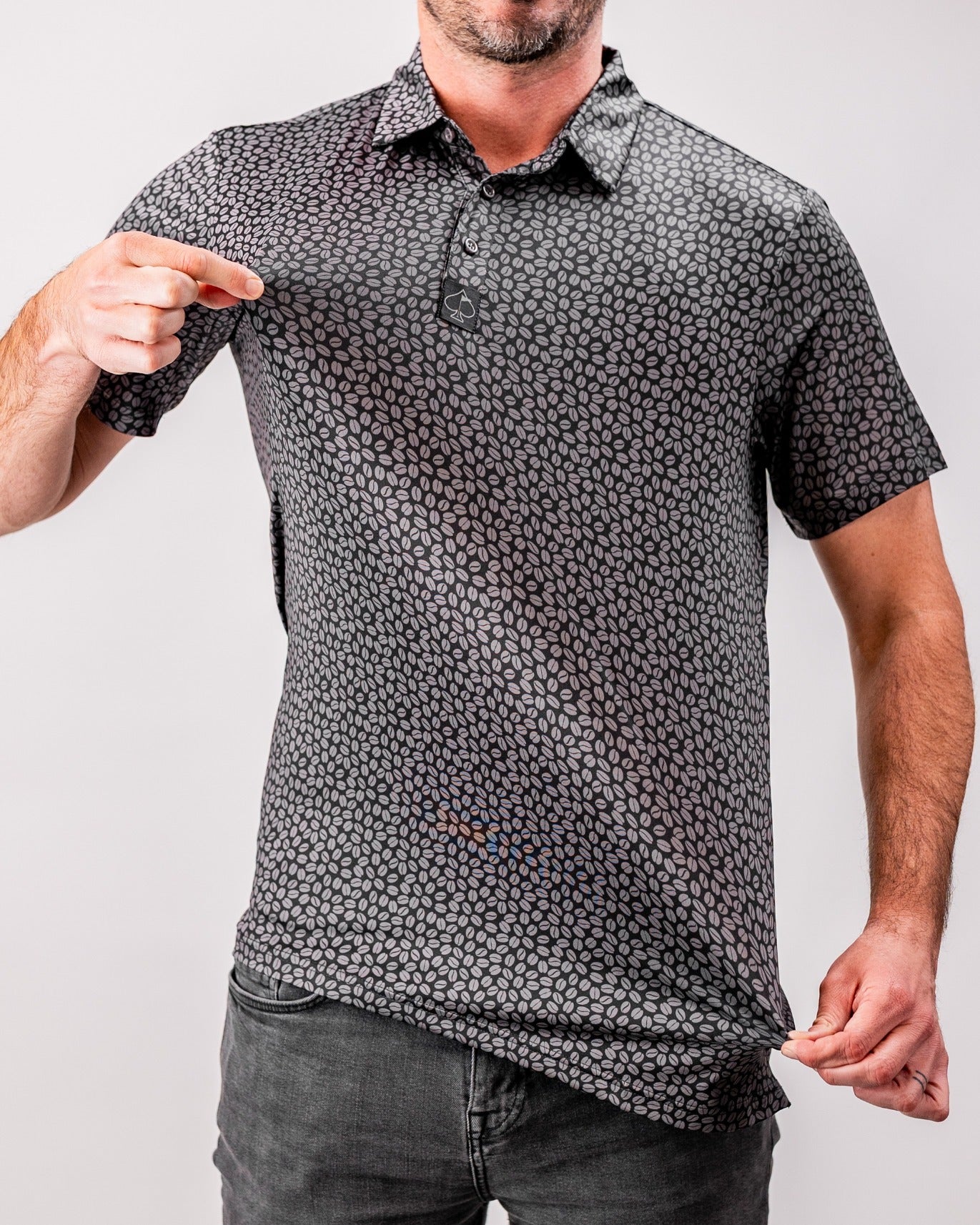 A man showcases a black polo shirt with a subtle coffee bean pattern, highlighting its stylish design and fit.