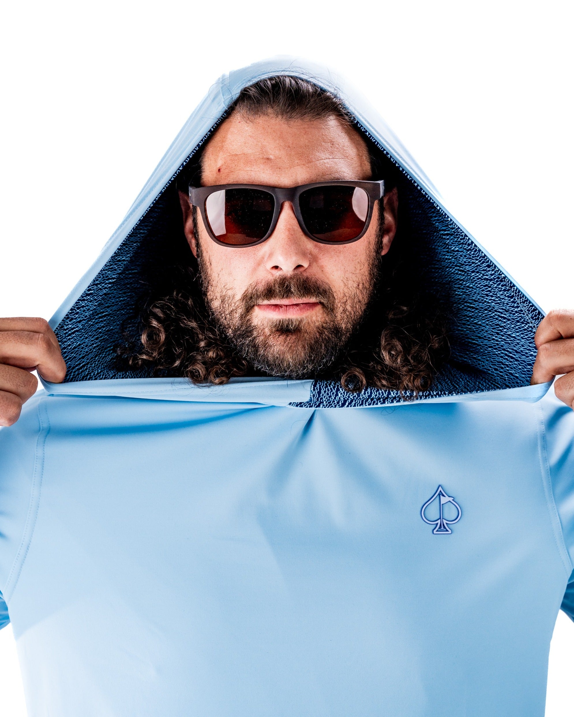 Man wearing a light blue performance golf hoodie with a hood up, showcasing a stylish design and sunglasses.