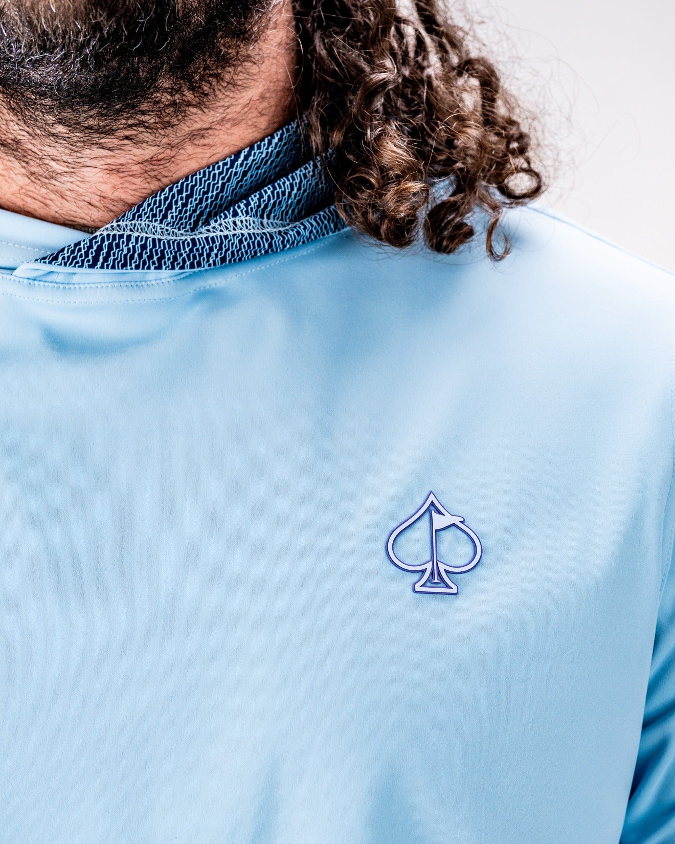 Light blue performance golf hoodie featuring a unique squiggle design and an embroidered spade logo on the chest.