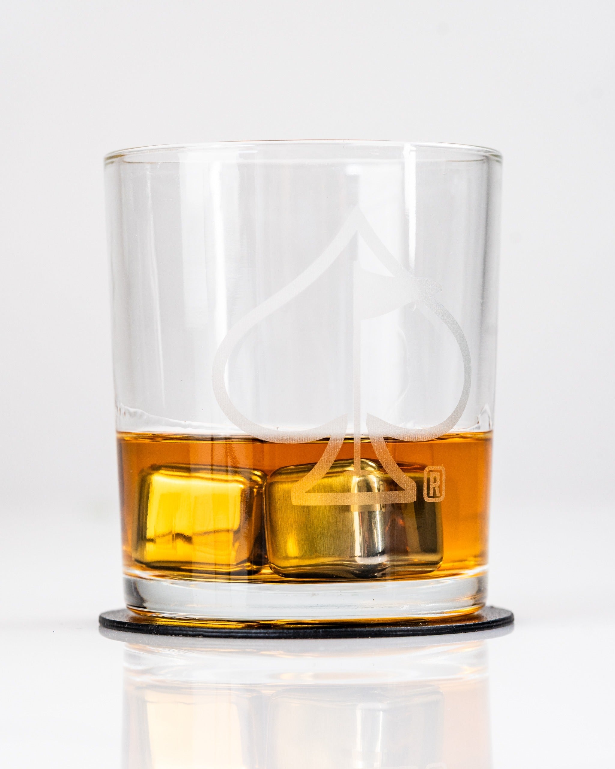 Set of 2 whisky glasses featuring a spade design, filled with amber whisky and ice cubes on a black coaster.