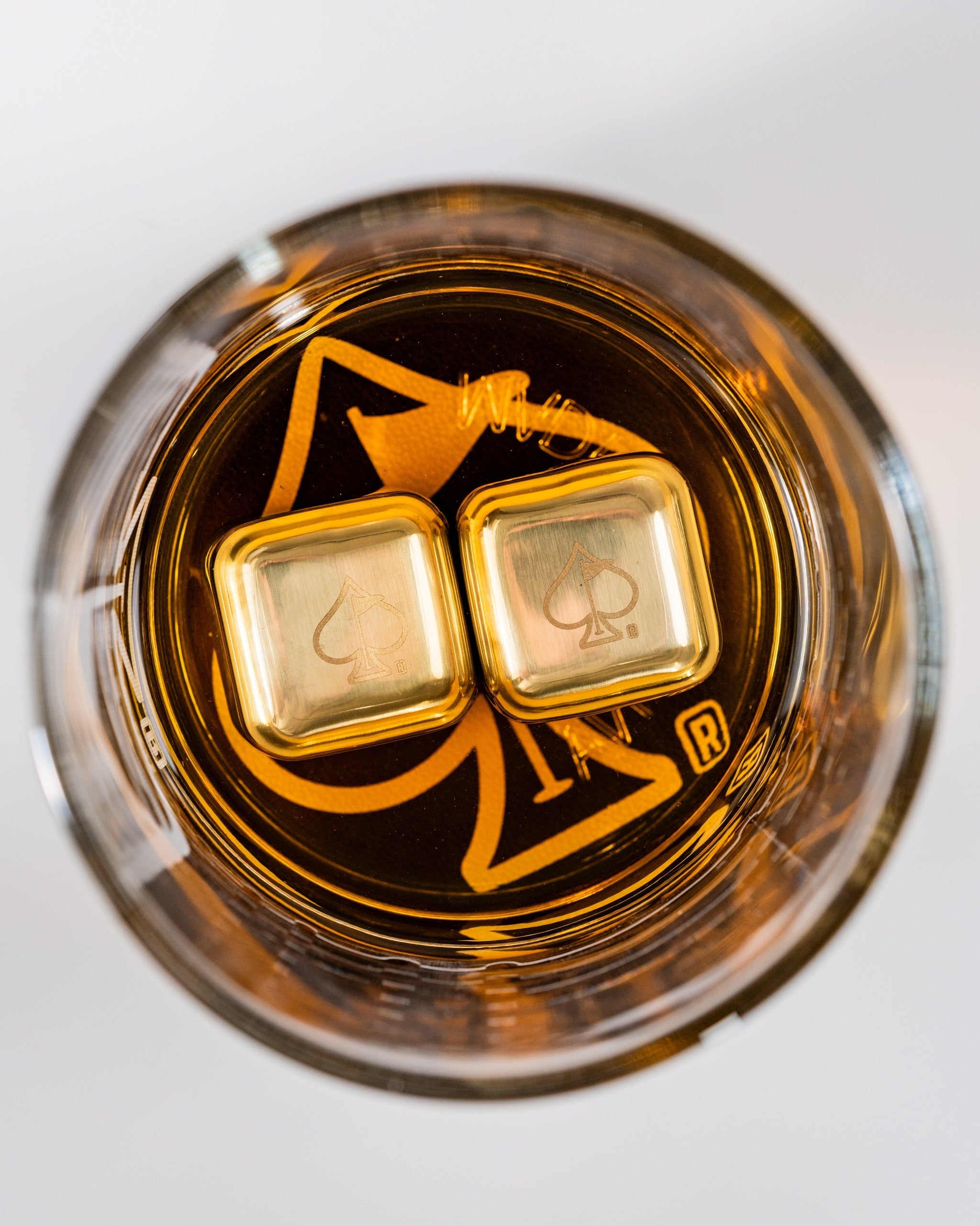 Set of two whisky glasses featuring a unique design, showcasing golden ice cubes in amber whisky.