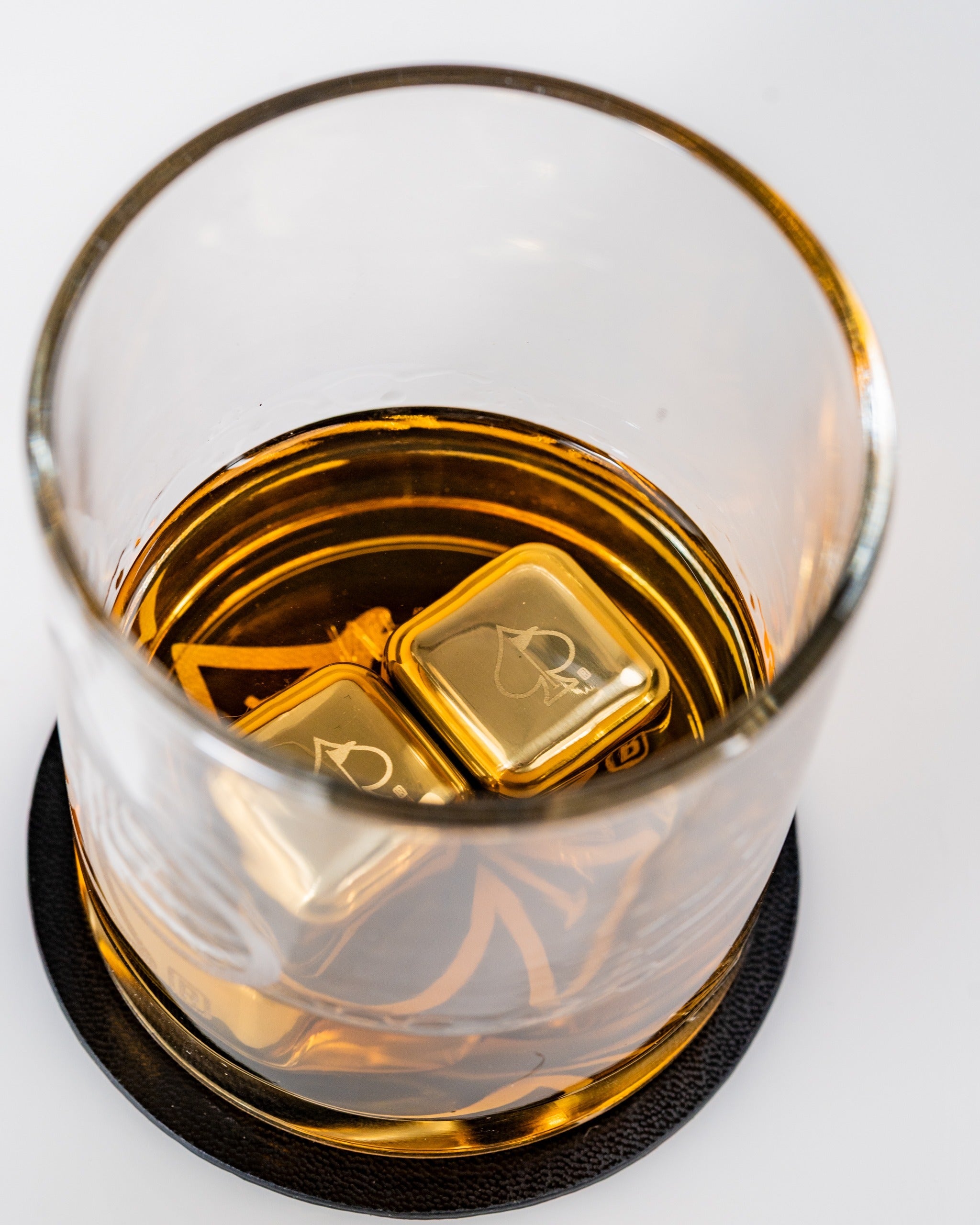 Set of two whisky glasses featuring gold-colored ice cubes, showcasing rich amber whisky on a stylish coaster.