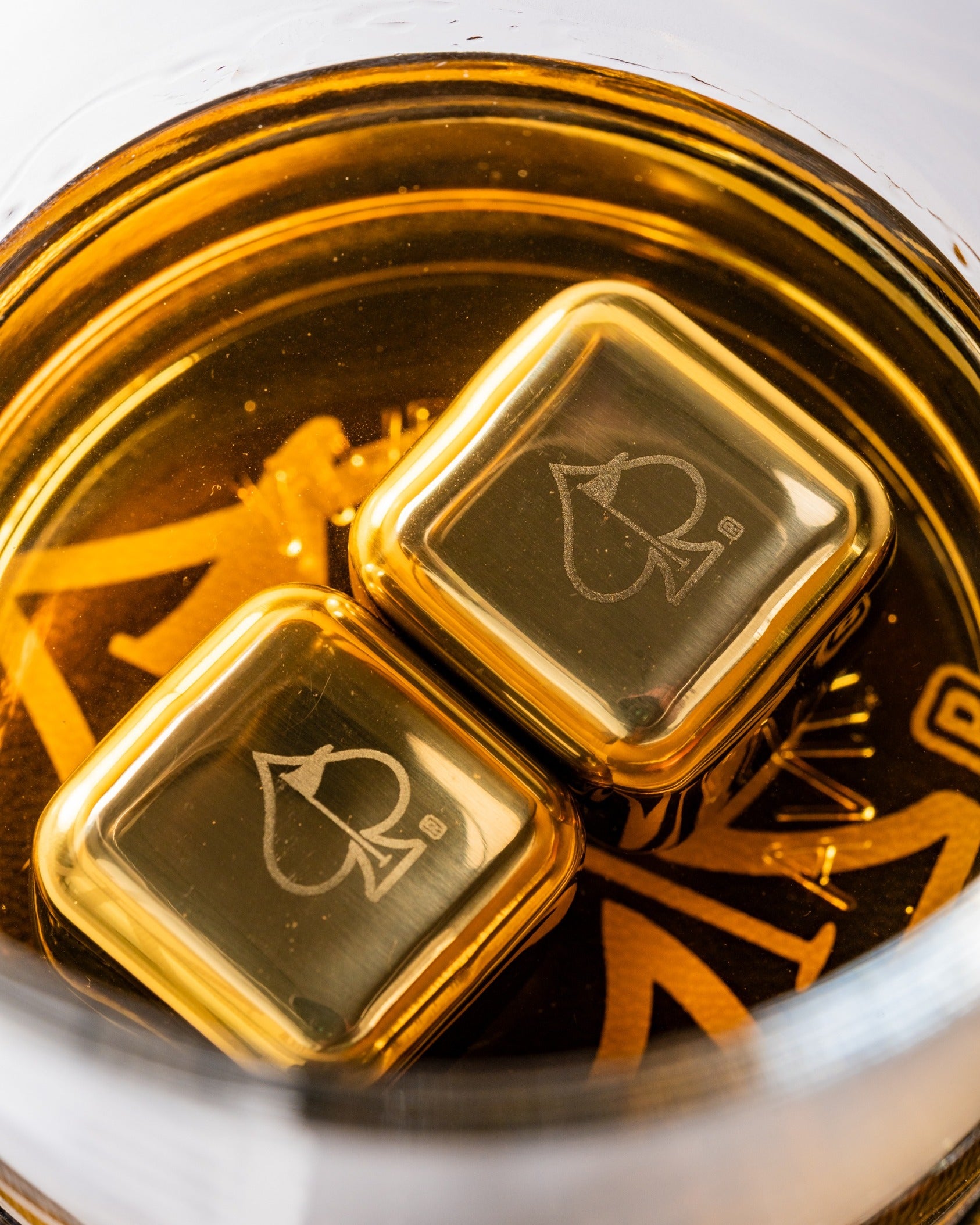 Set of two whisky glasses featuring gold square ice cubes, showcasing rich amber whisky inside.