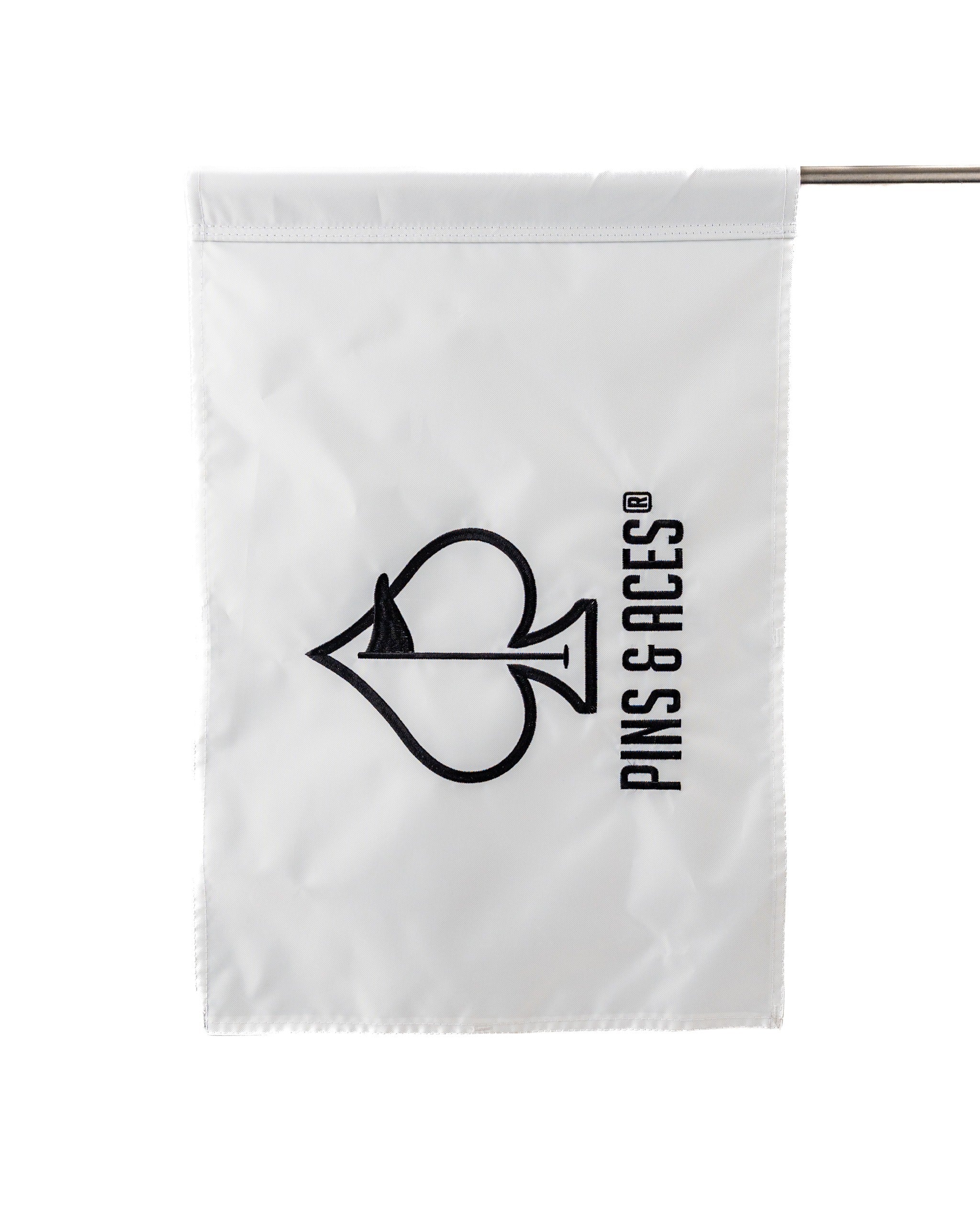 White golf flag featuring a black spade logo and "PINS & ACES" text, designed for stylish golf courses.