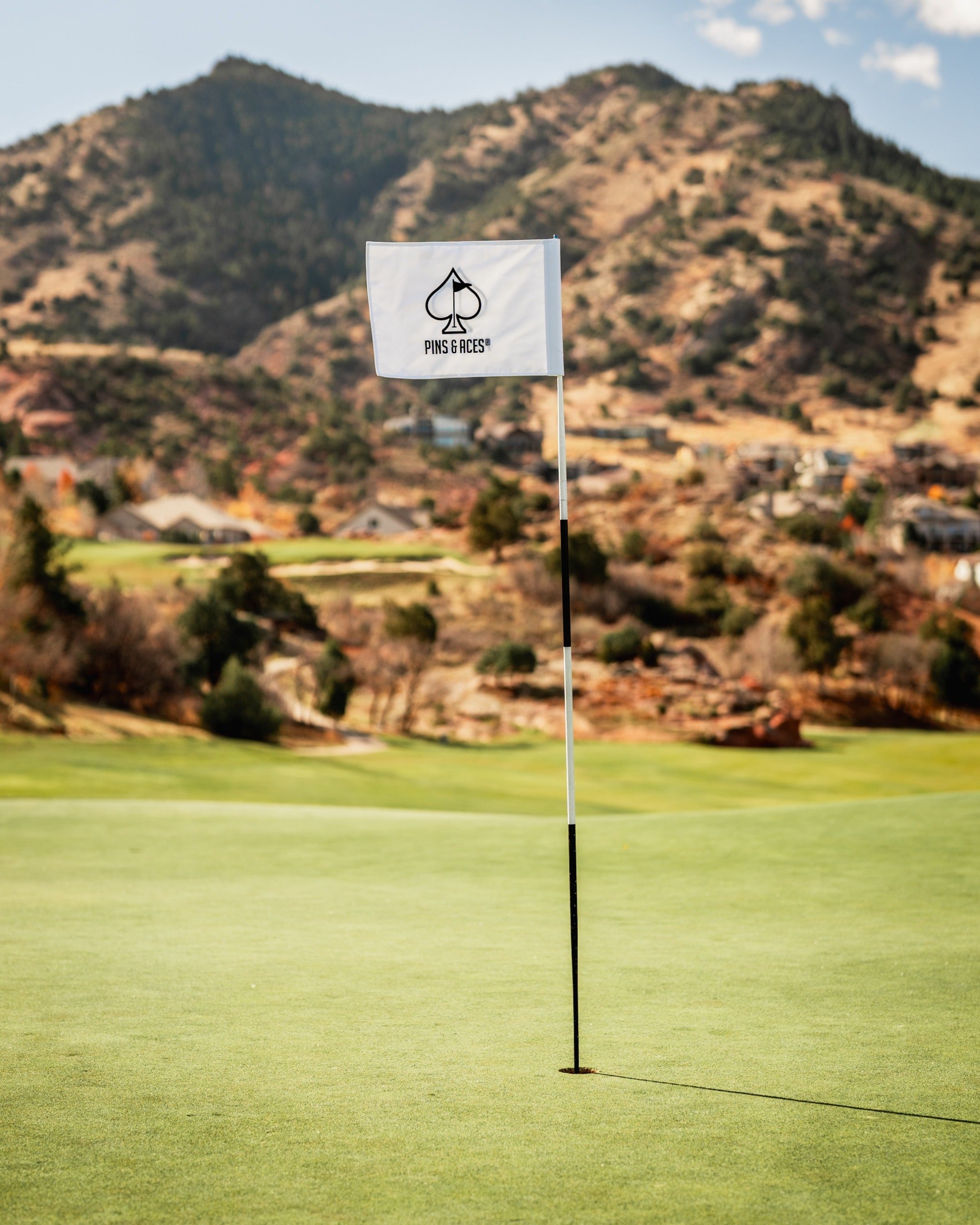 Golf flag featuring the Pins and Aces logo, set against a scenic mountainous landscape on a golf course.
