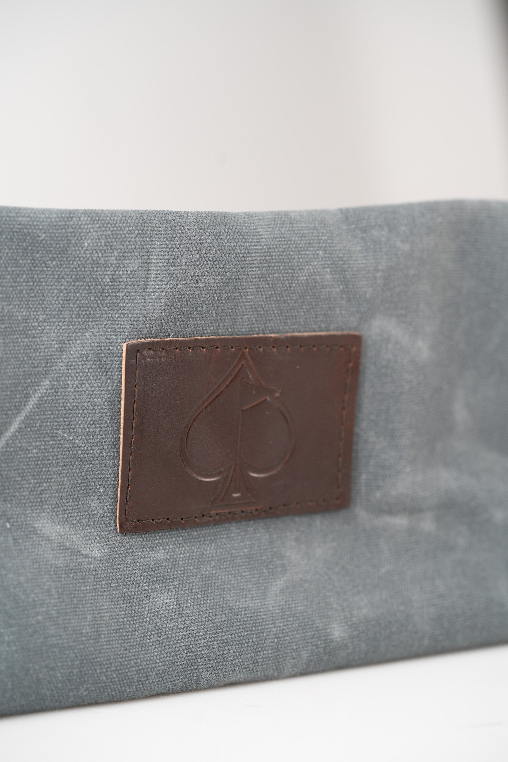 Stylish gray toiletry bag featuring a leather patch with an embossed spade logo, perfect for organizing grooming essentials.