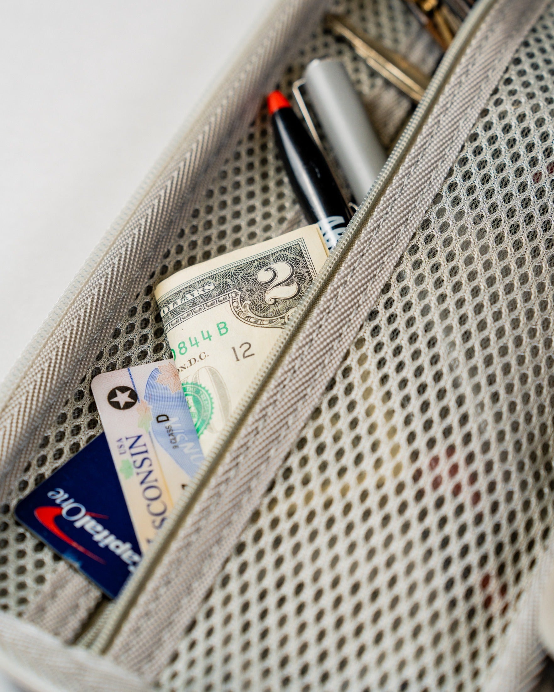 Gray glove and accessory caddie featuring a mesh design, holding cash, a credit card, and pens for convenient storage.