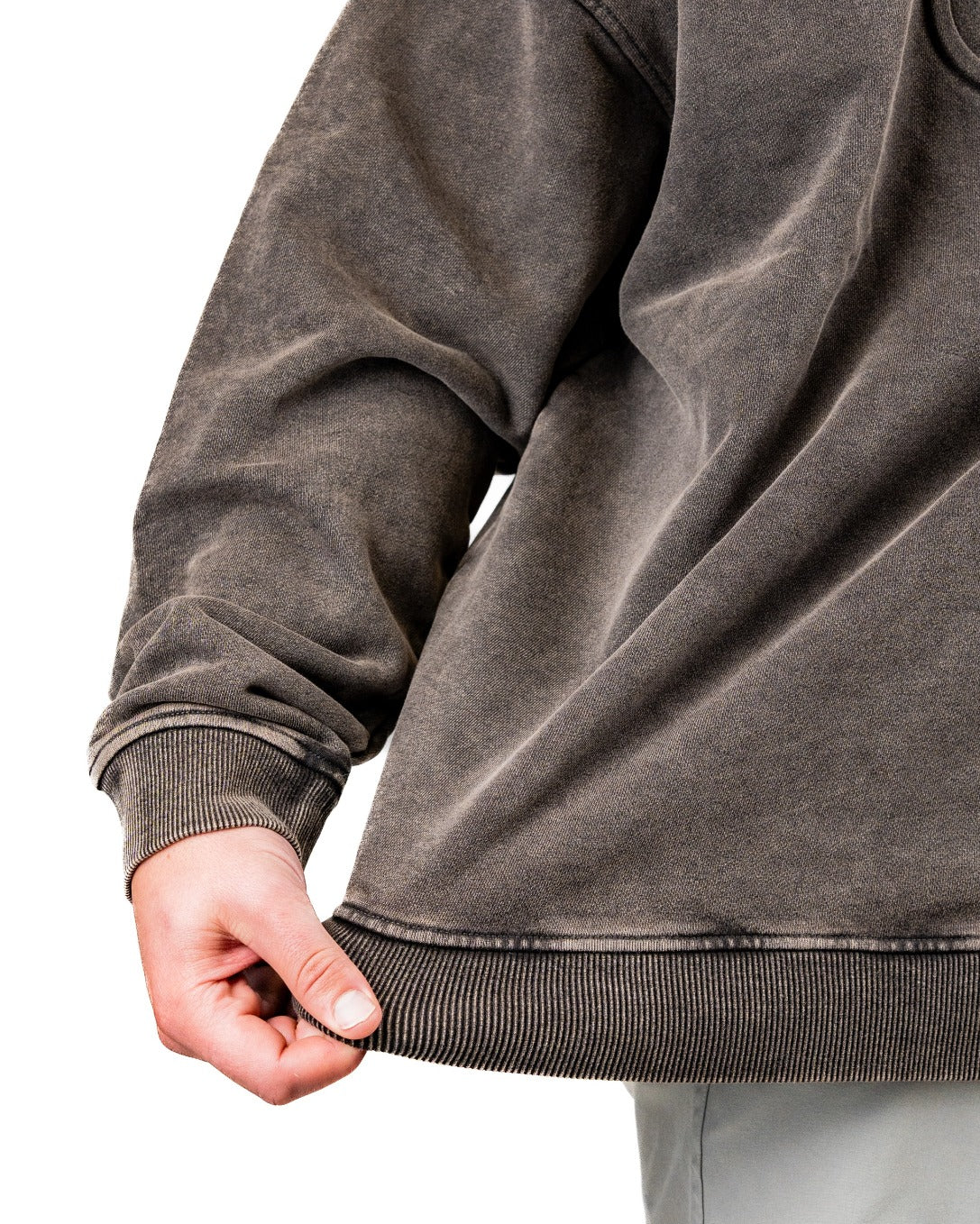 Close-up of a person holding the hem of an embossed spade crewneck sweatshirt in washed iron color, showcasing its texture.