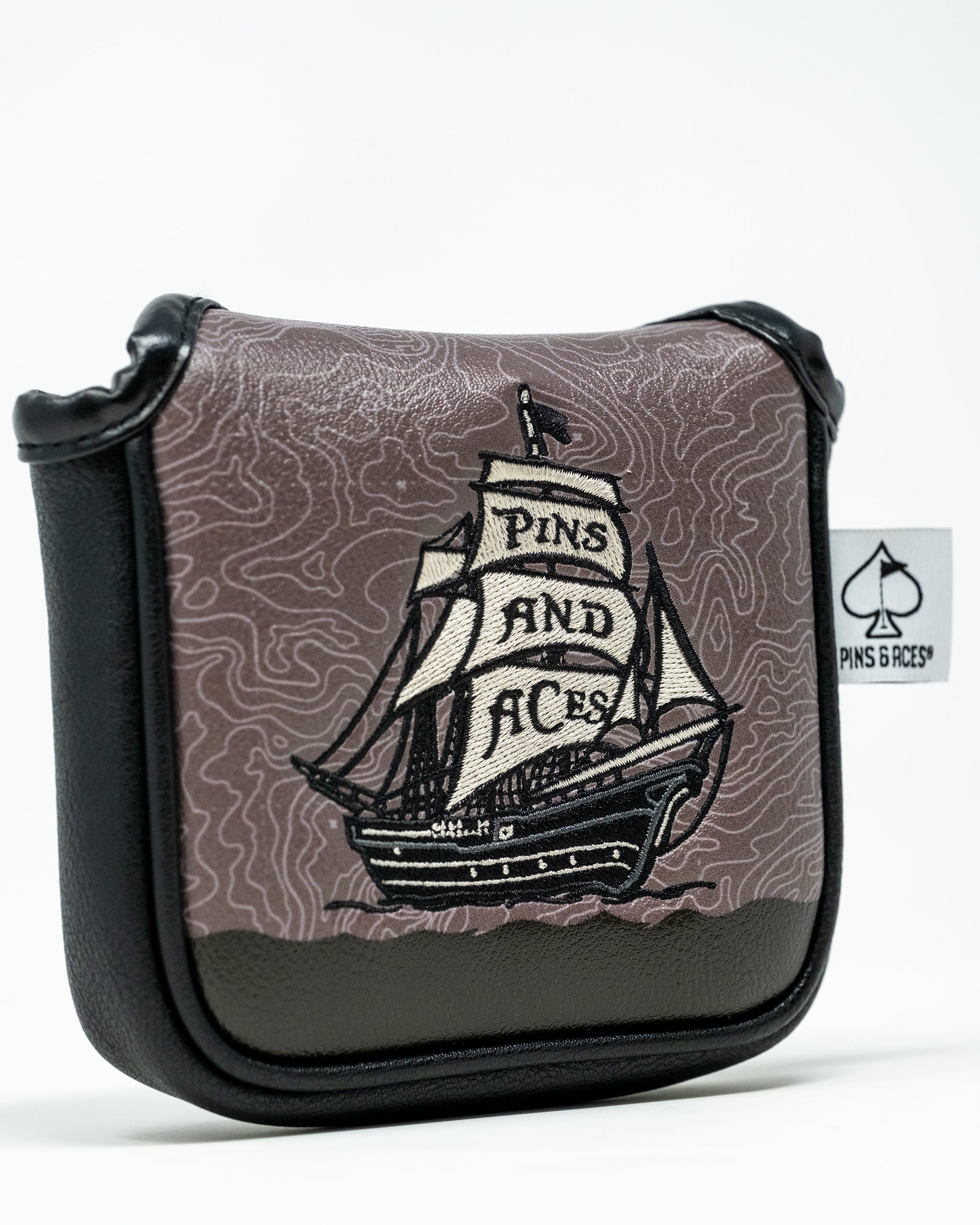 Bold brown and black golf accessory pouch with embroidered sailboat and "PINS AND ACES" banner, featuring topographic map ...