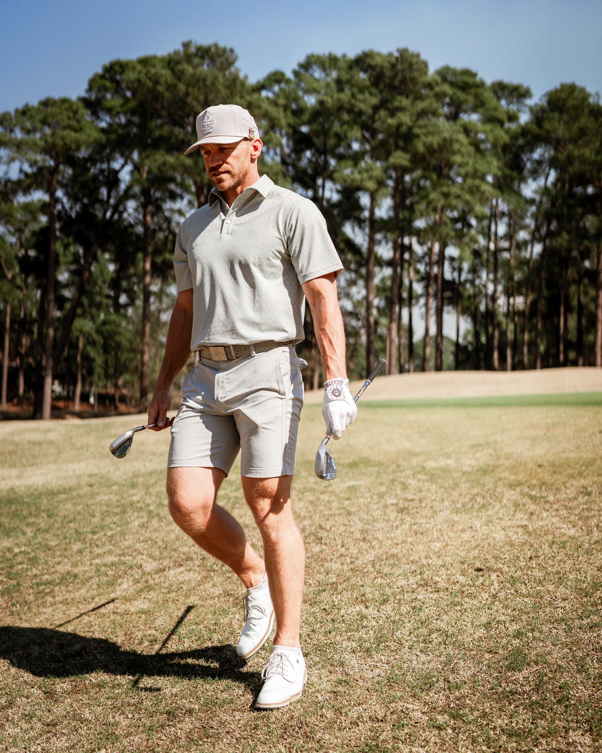 A golfer walks on the course wearing a light gray polo and shorts, showcasing a stylish and modern golf outfit.
