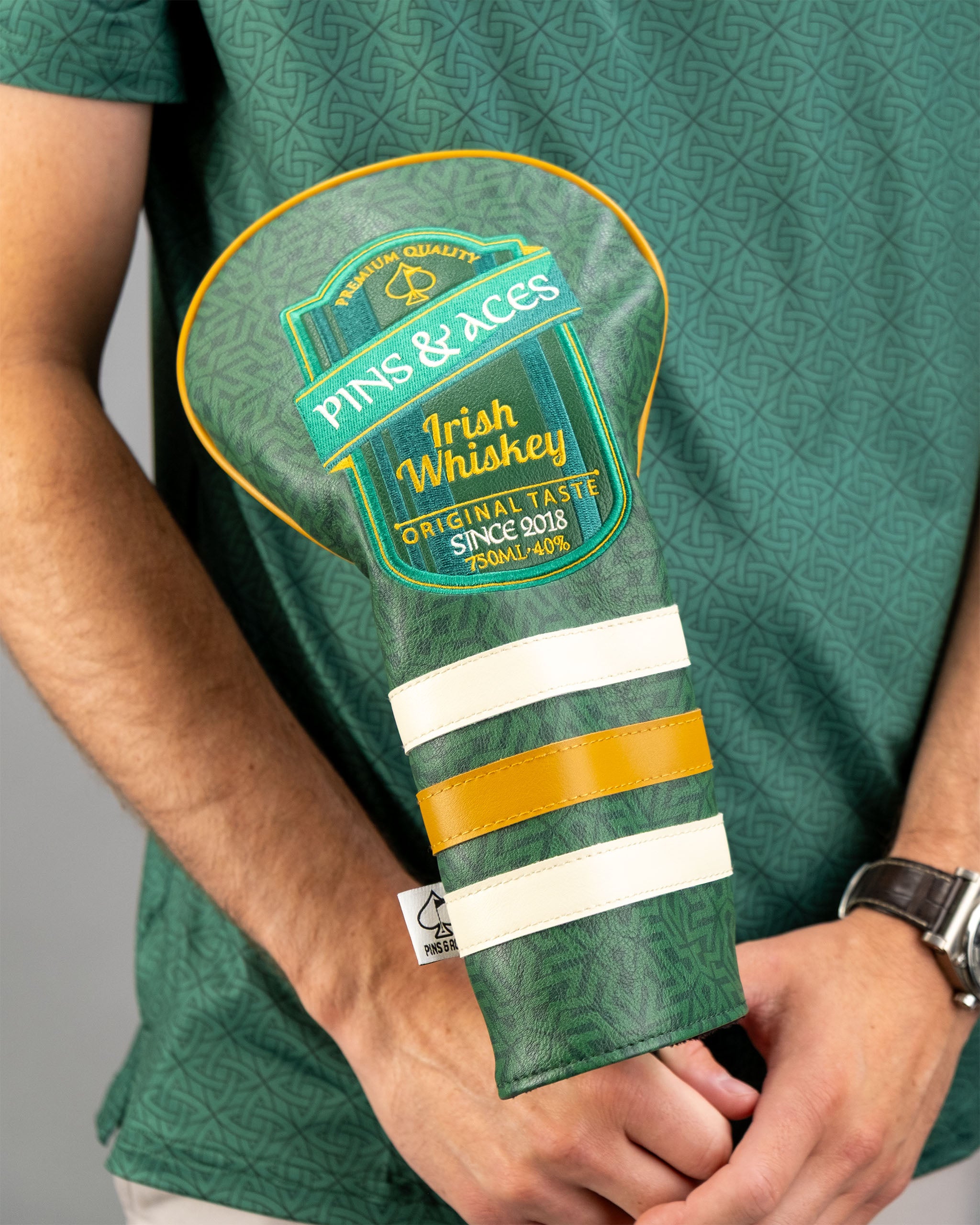 Emerald Links golf headcover featuring a green design with yellow and white stripes, held by a person.