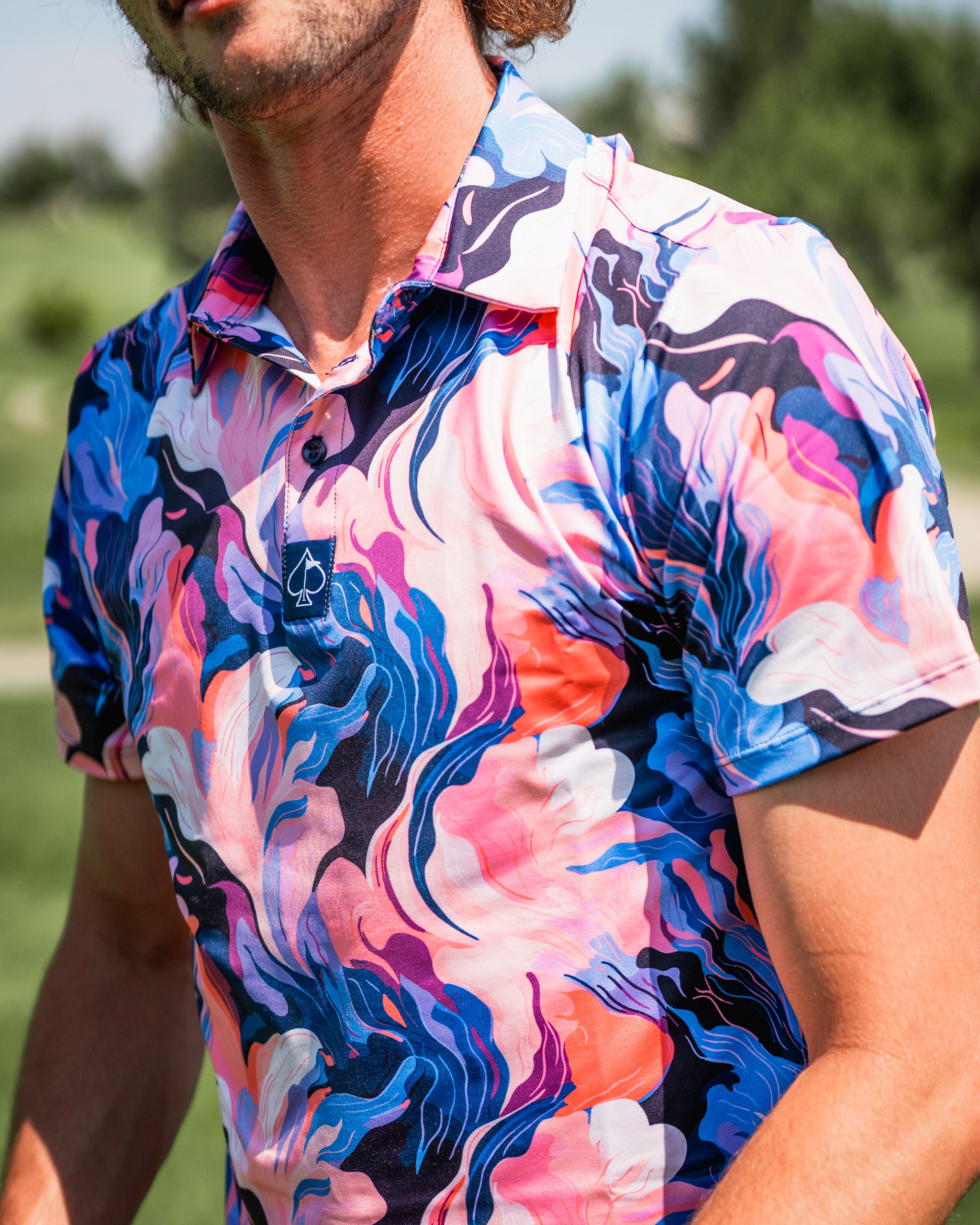 A man wearing a vibrant Melting Floral golf shirt featuring bold, swirling patterns in pink, blue, and white.