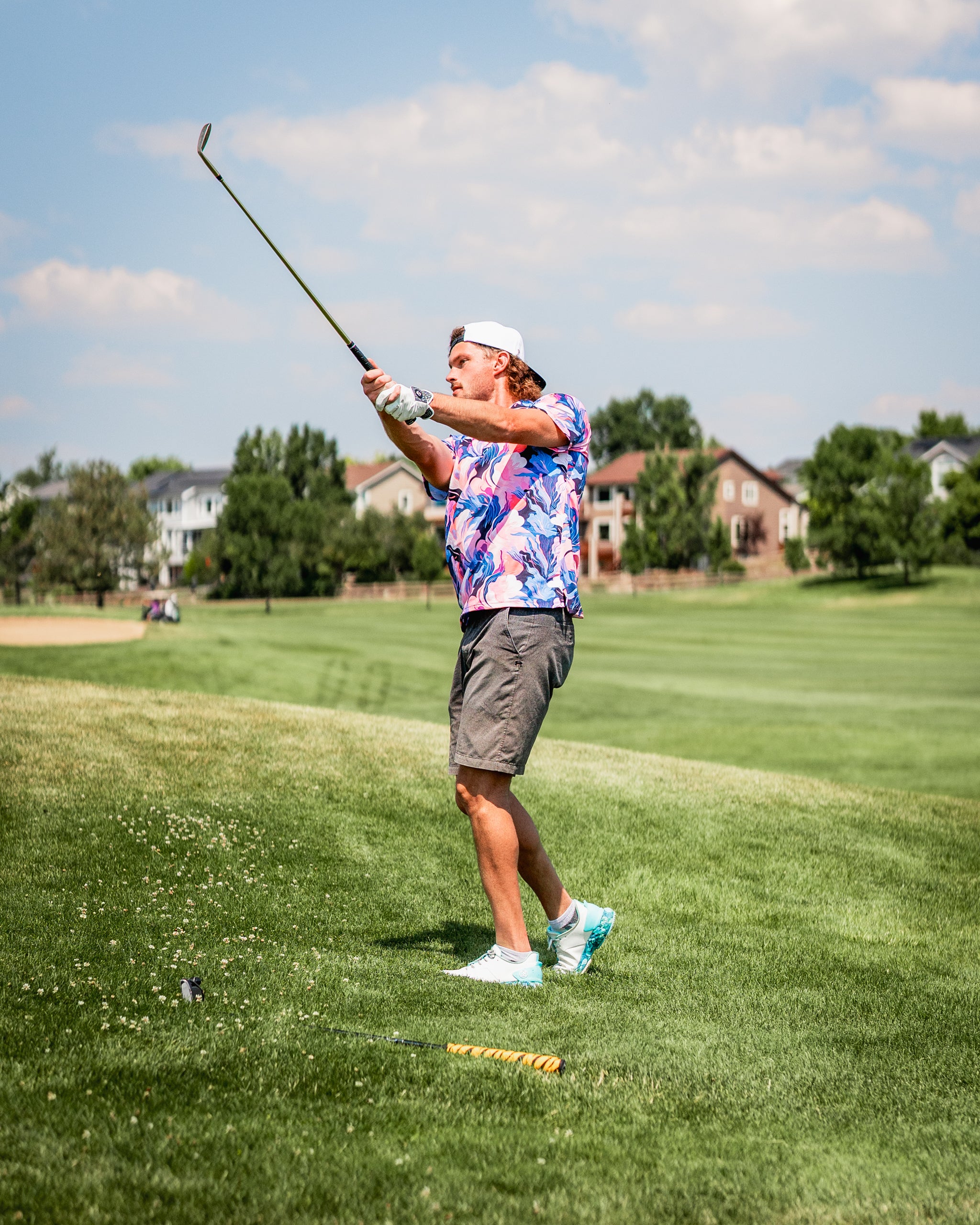 Golfer in a melting floral shirt swings a club on a sunny course, showcasing bold style and vibrant colors.