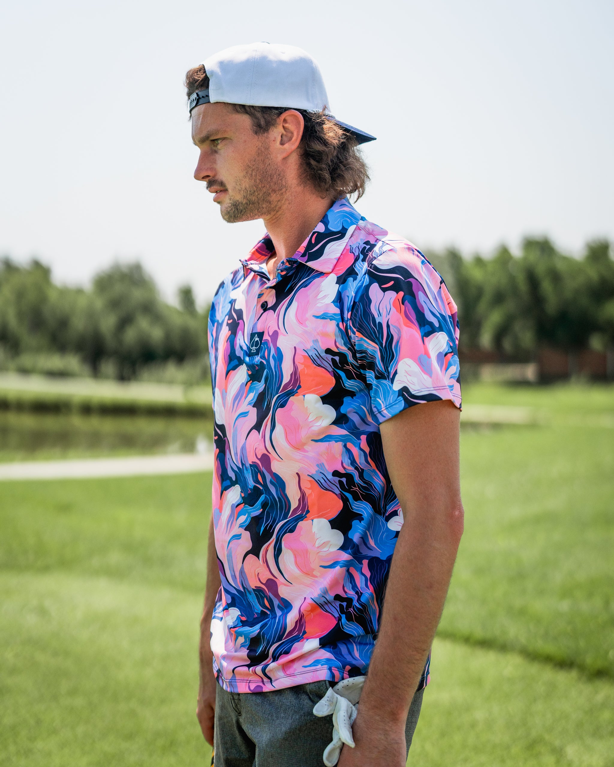 A golfer wearing a vibrant Melting Floral polo shirt with swirling pink and blue patterns, standing on a lush green course.