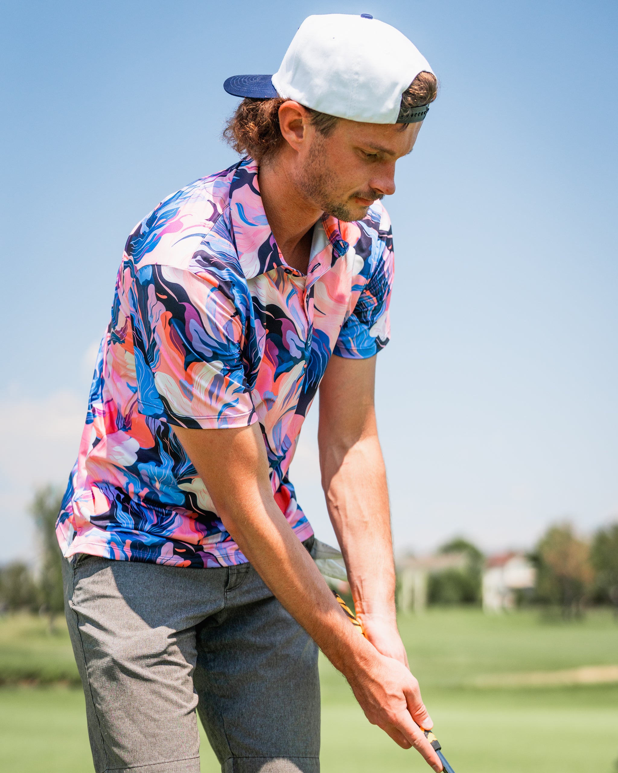 A golfer wearing a vibrant Melting Floral polo shirt in pink and blue, preparing to putt on a sunny course.