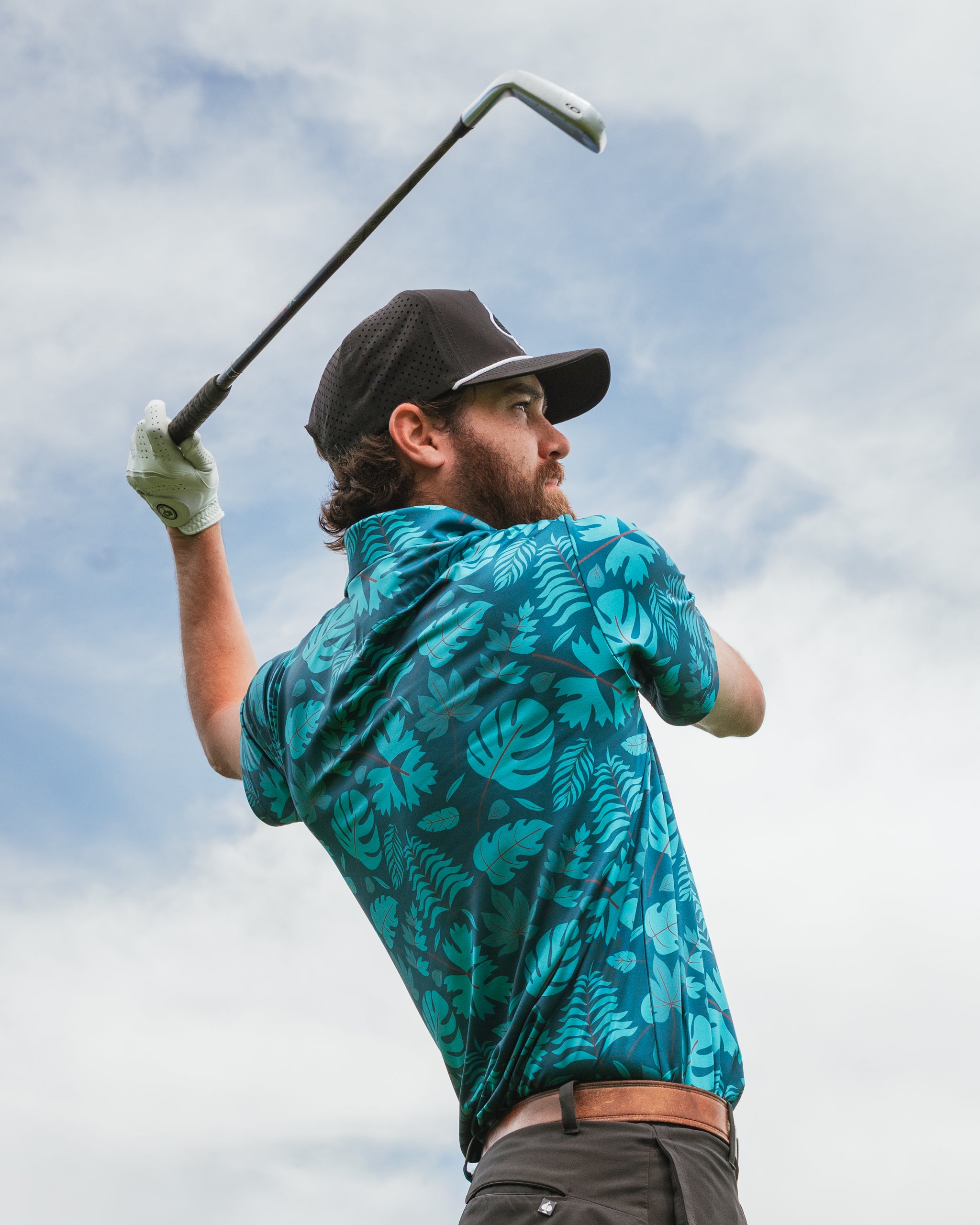 A golfer swings a club while wearing a vibrant, tropical-patterned shirt, showcasing bold style on the course.