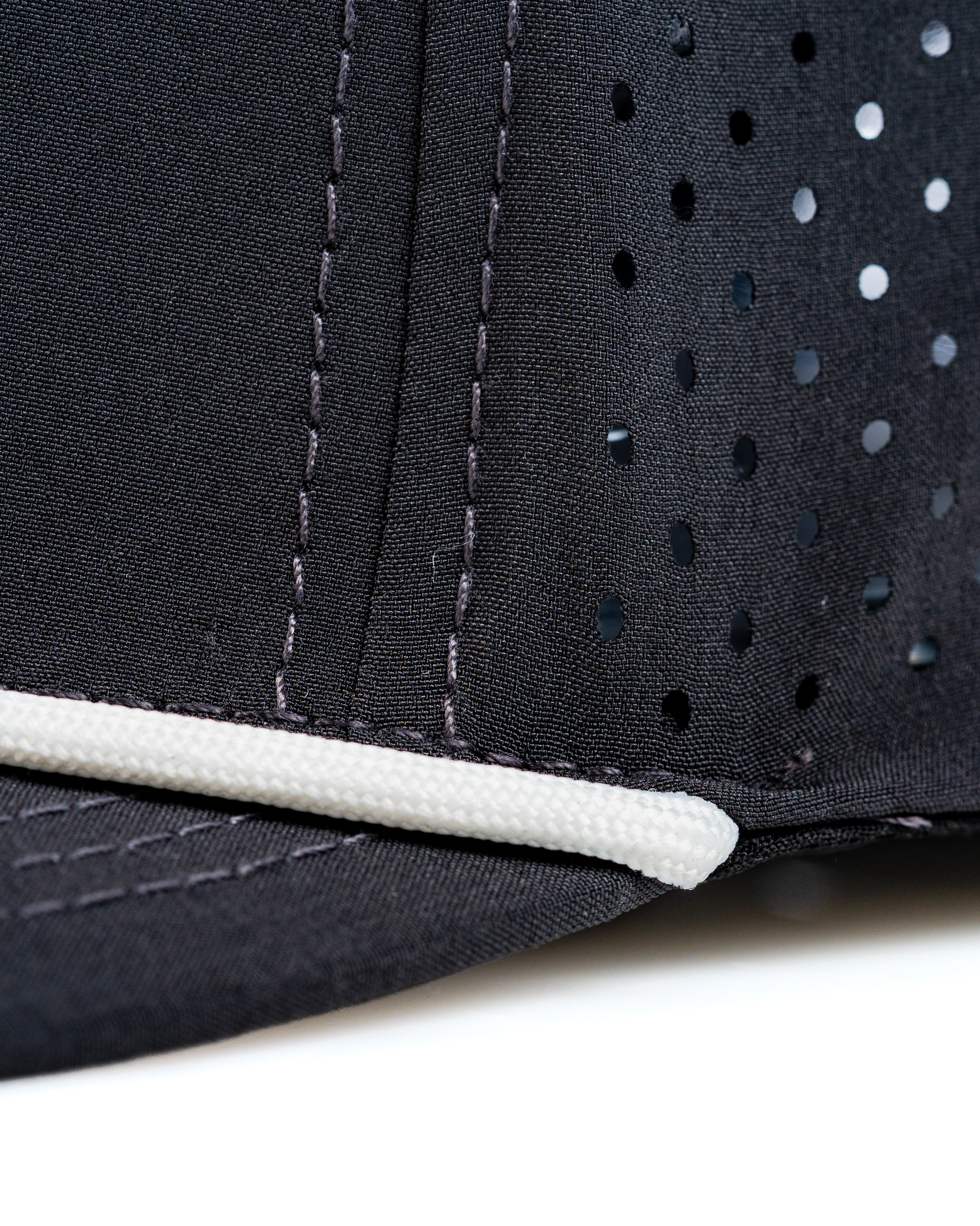 Close-up of the Perforated Rope Hat in Butter Cut, featuring a black fabric with perforations and a white rope detail.