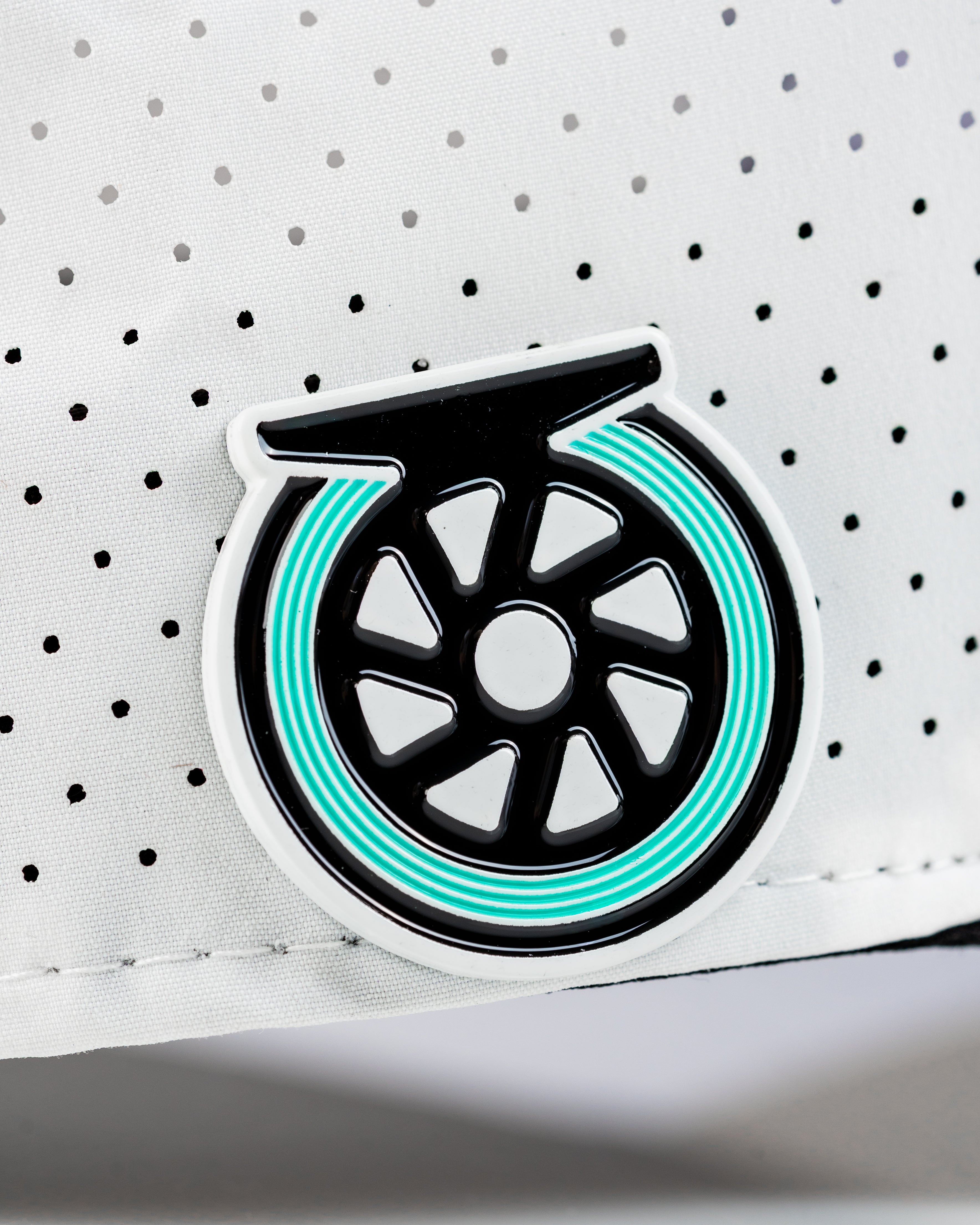 Close-up of the Tradesman Hat featuring a unique reel logo on a white perforated fabric background.