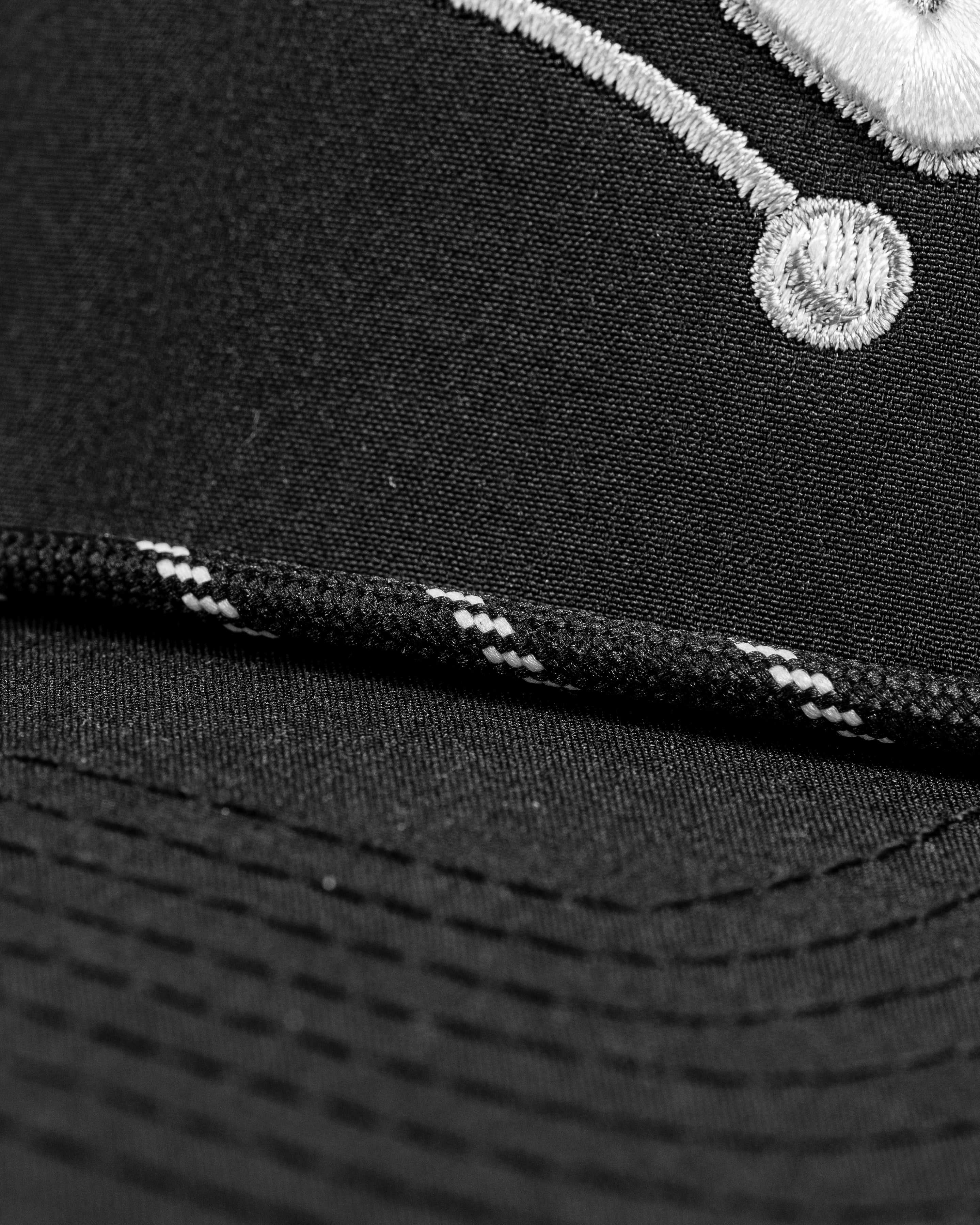 Close-up of the Perforated Rope Hat - Slice, featuring a black fabric with white embroidered details and a stylish rope accent.