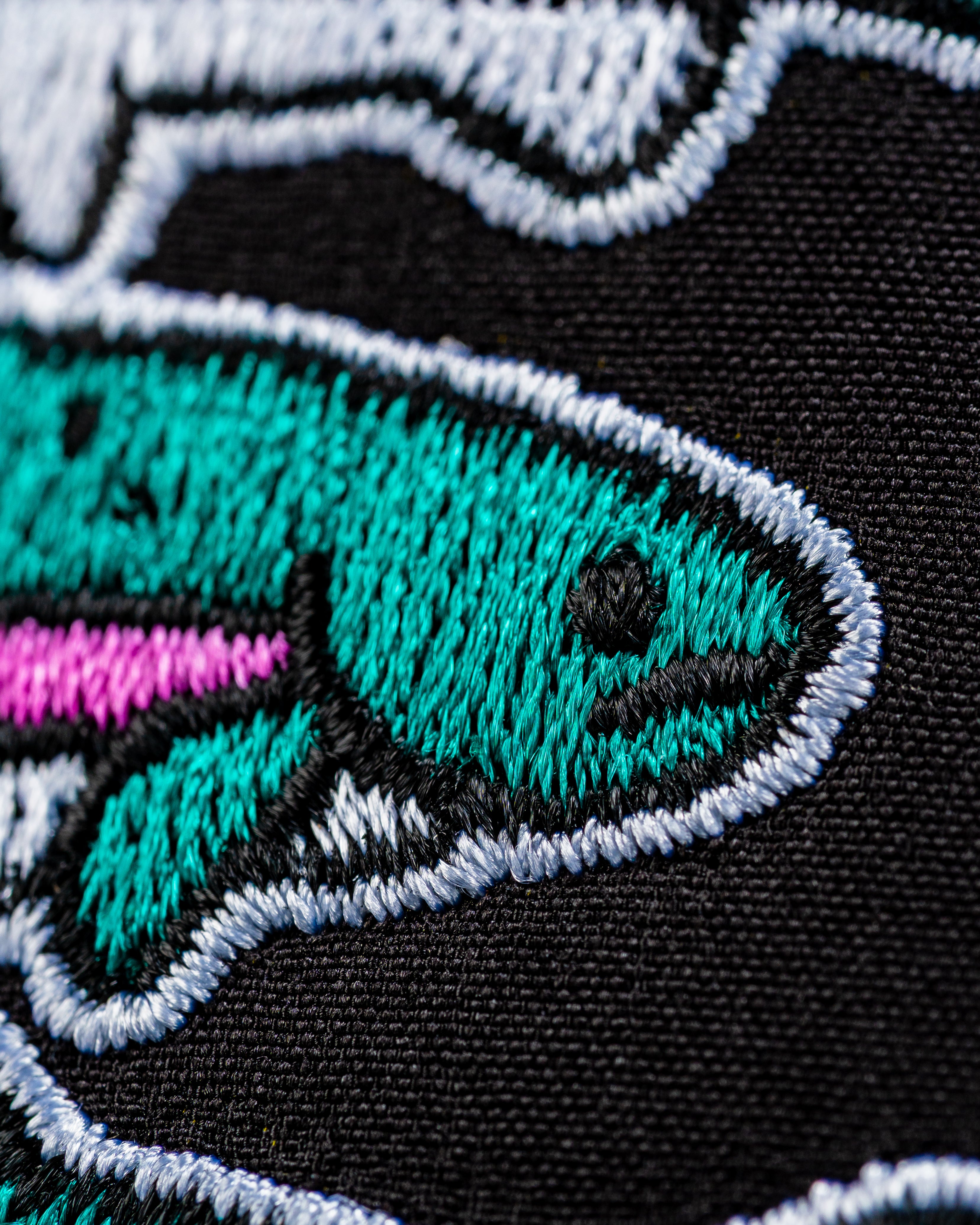 Close-up of the embroidered design on the Perforated Rope Hat featuring colorful fish on a black background.