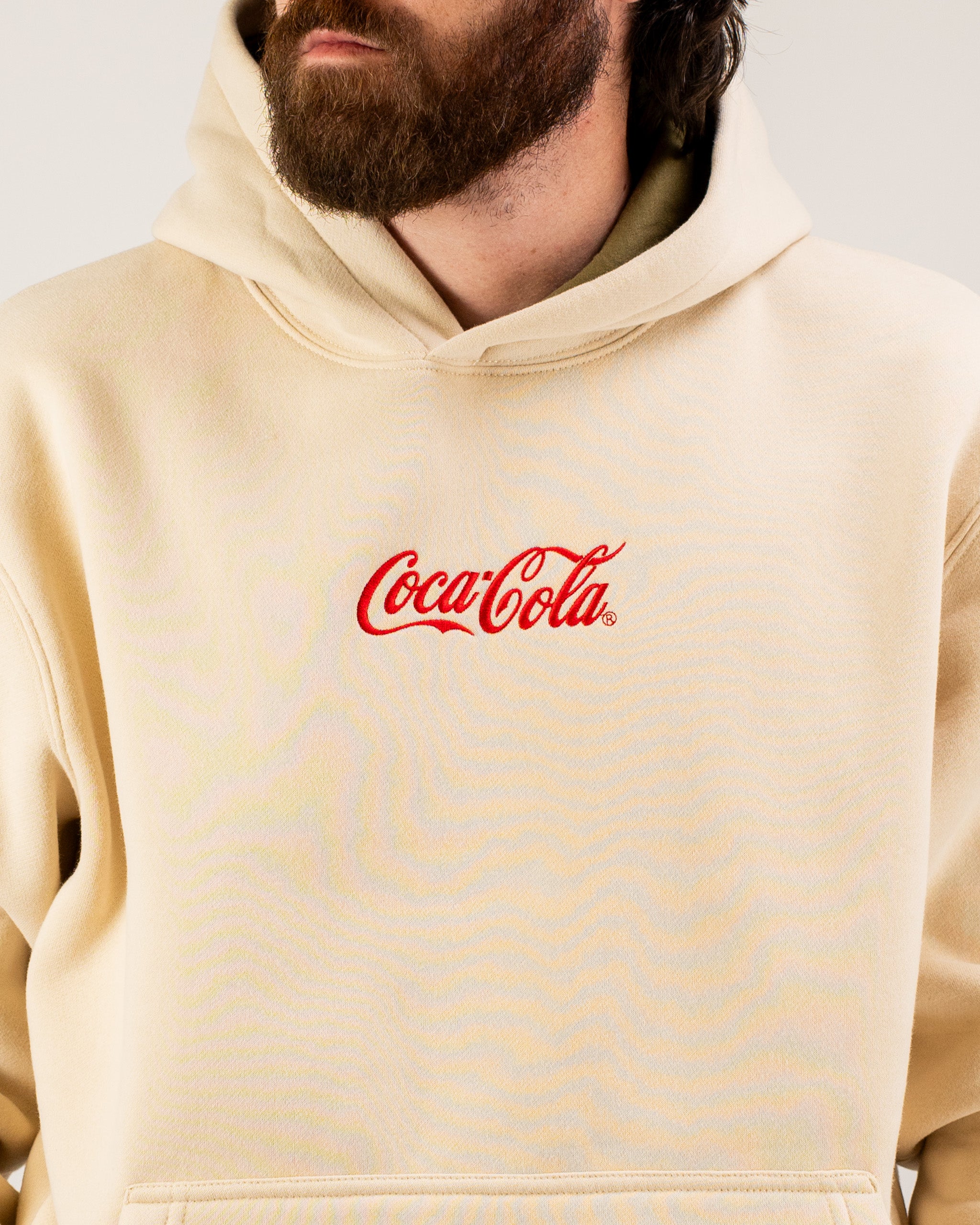 Beige lifestyle hoodie featuring a classic Coca-Cola logo in red, perfect for casual wear and showcasing brand style.