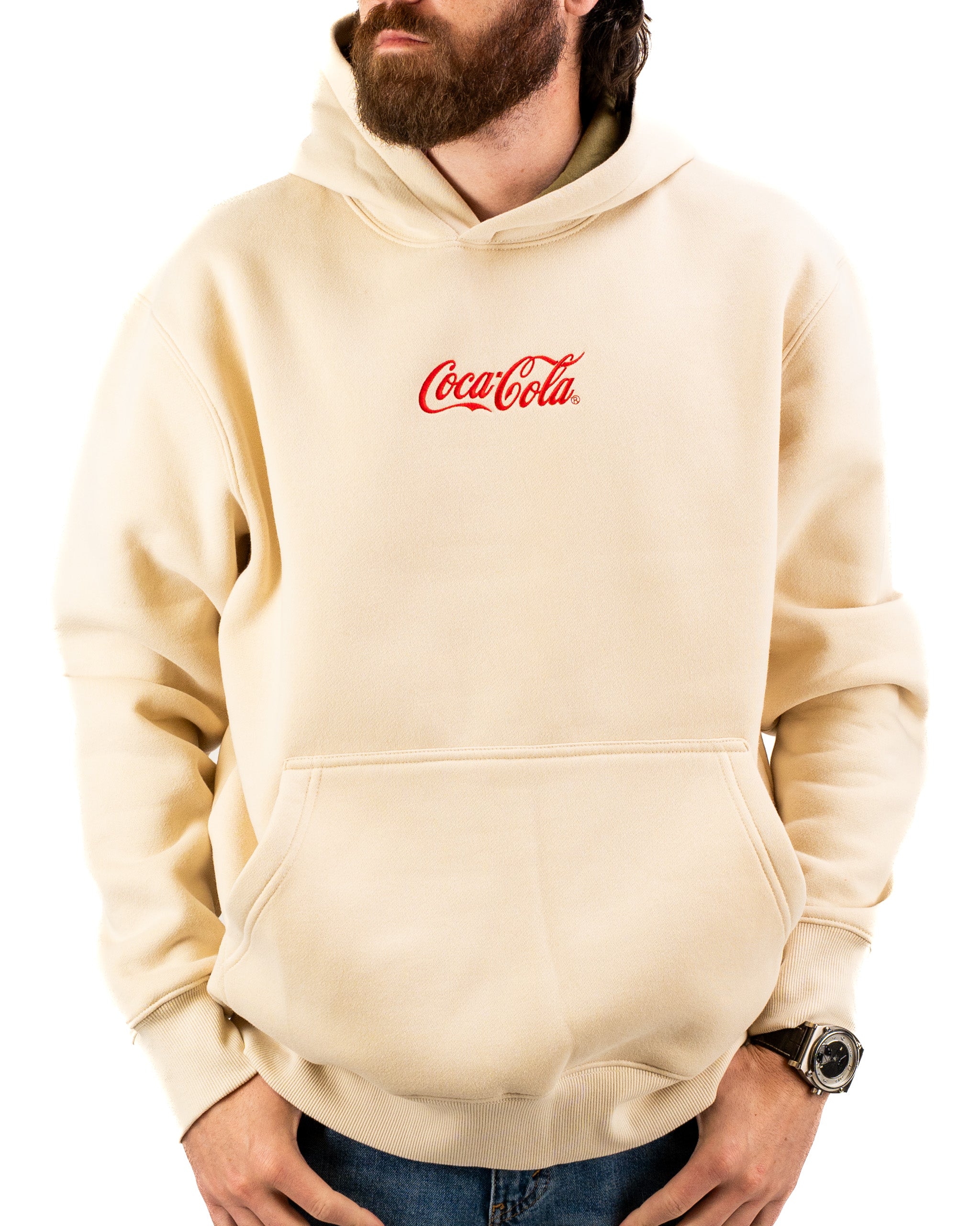 Beige lifestyle hoodie featuring a classic Coca-Cola logo on the chest, worn by a man with a beard.