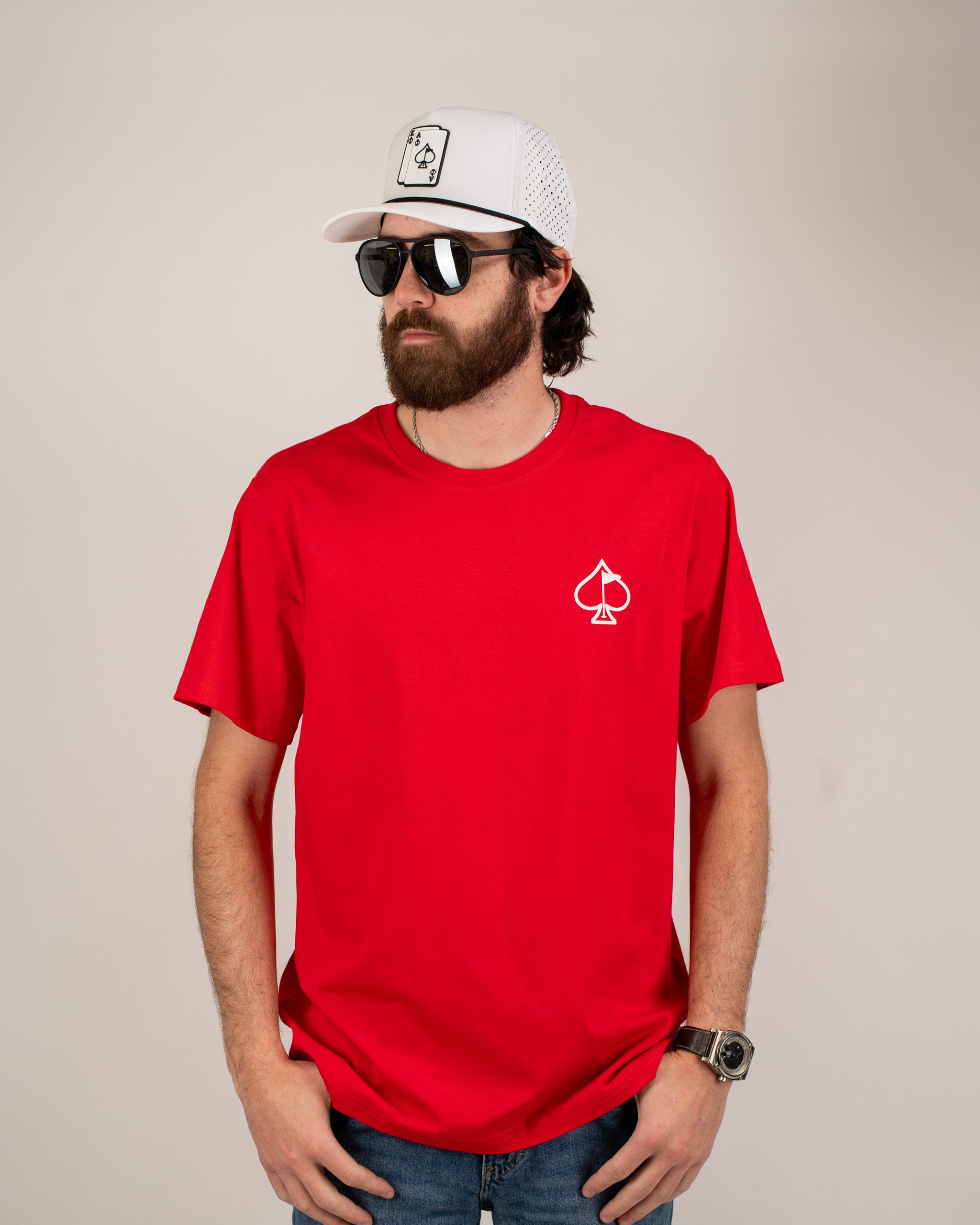 Bold red tee shirt featuring a white spade logo on the chest, styled with sunglasses and a cap for a trendy look.
