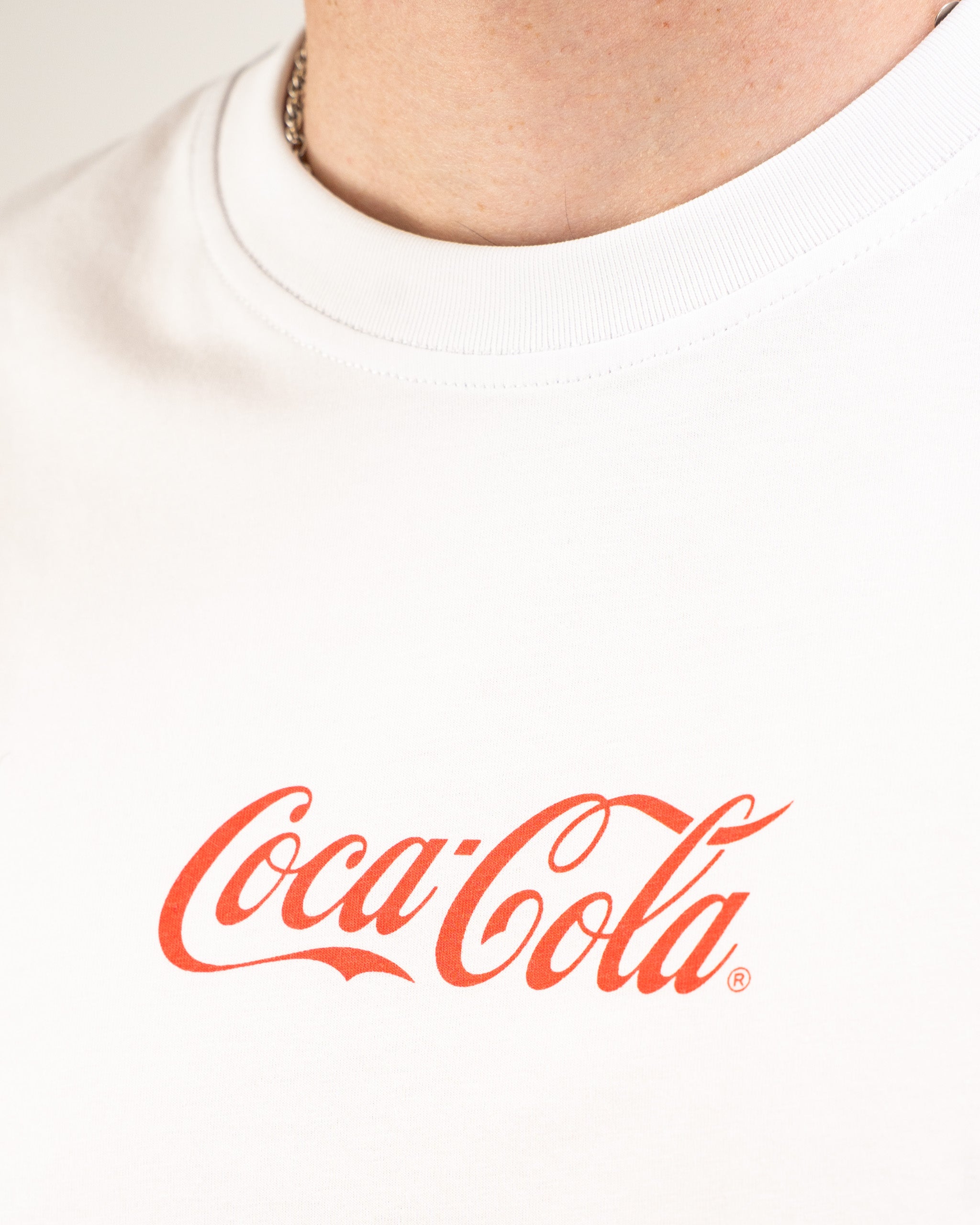 White tee shirt featuring a bold red Coca-Cola logo on the chest, perfect for casual wear and brand enthusiasts.