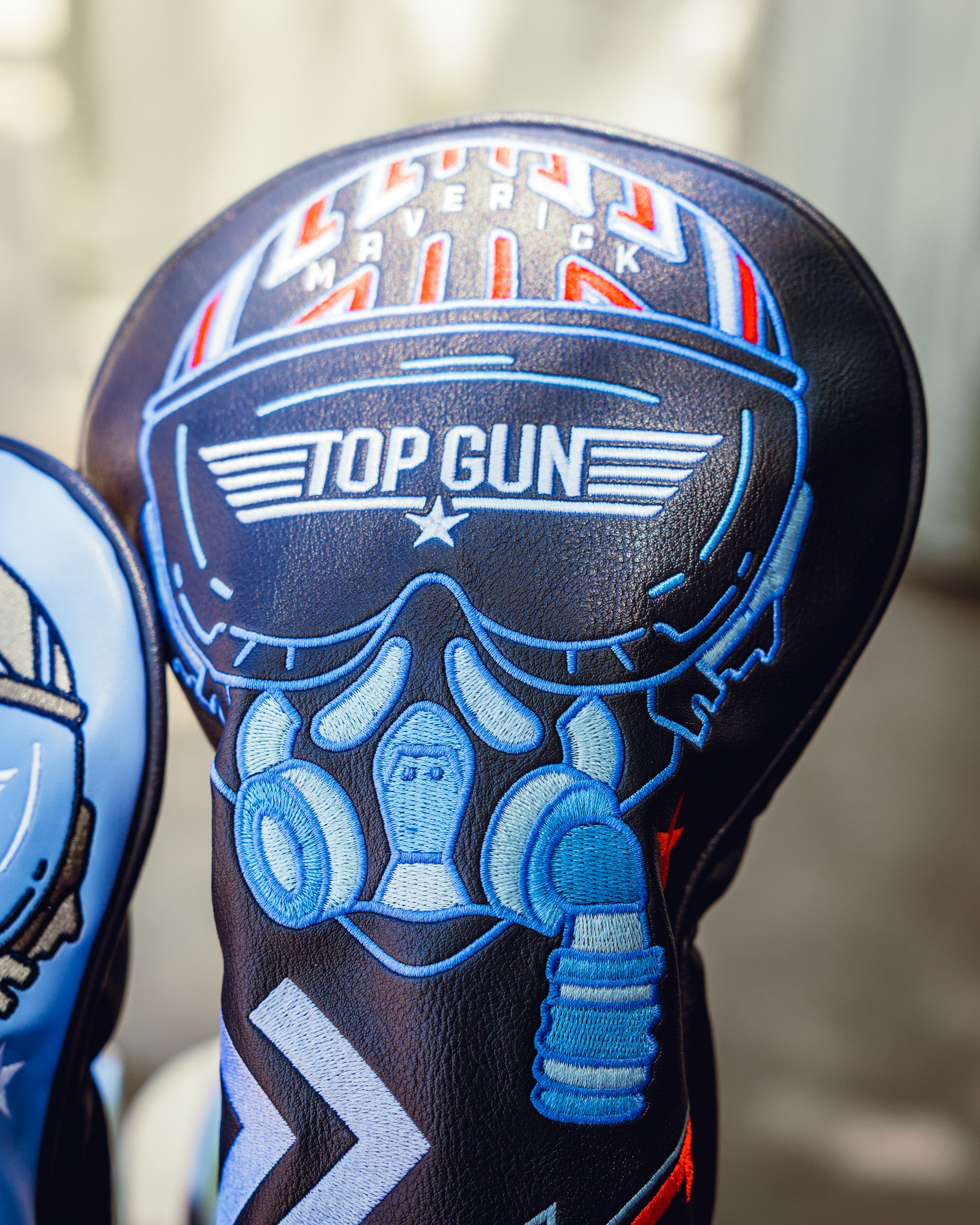 Bold black golf headcover with blue, white, and red "Top Gun" and skull design, featuring aviator goggles and helmet.