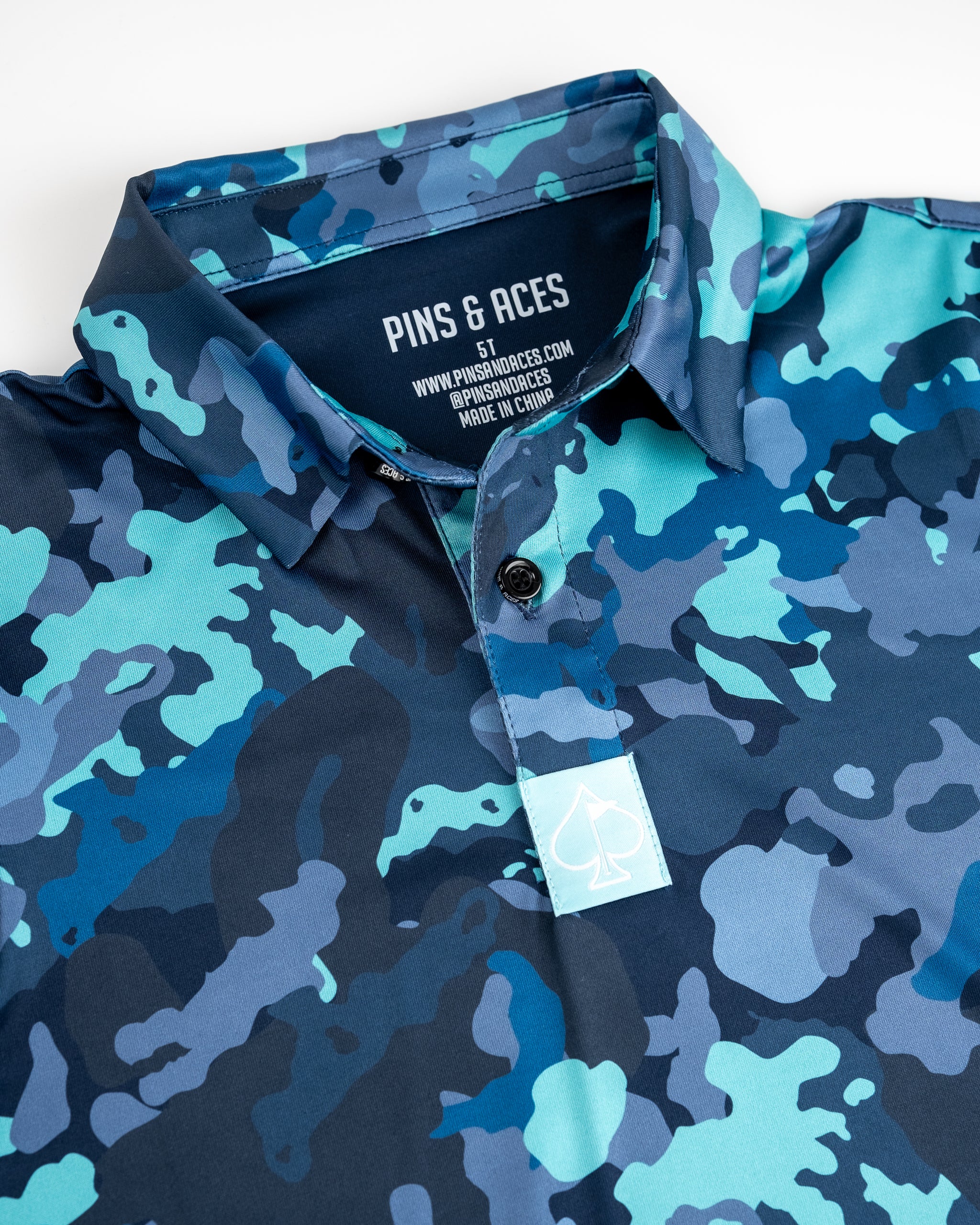 Youth electric camo patterned golf shirt with blue, teal, and navy camouflage print and a collar.