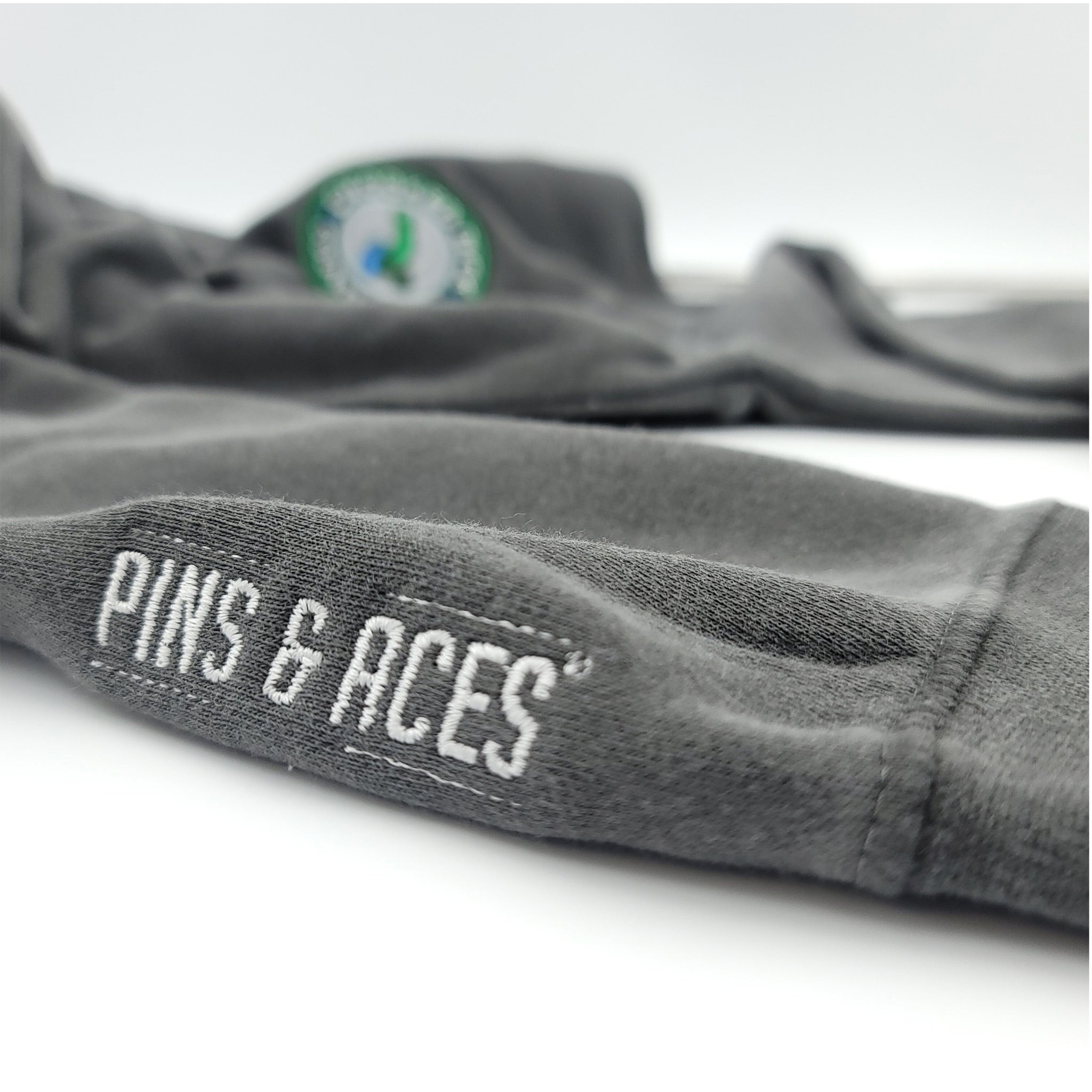 Close-up of a dark gray golf glove with "PINS & ACES" embroidered in white on the wrist, highlighting bold branding and sp...