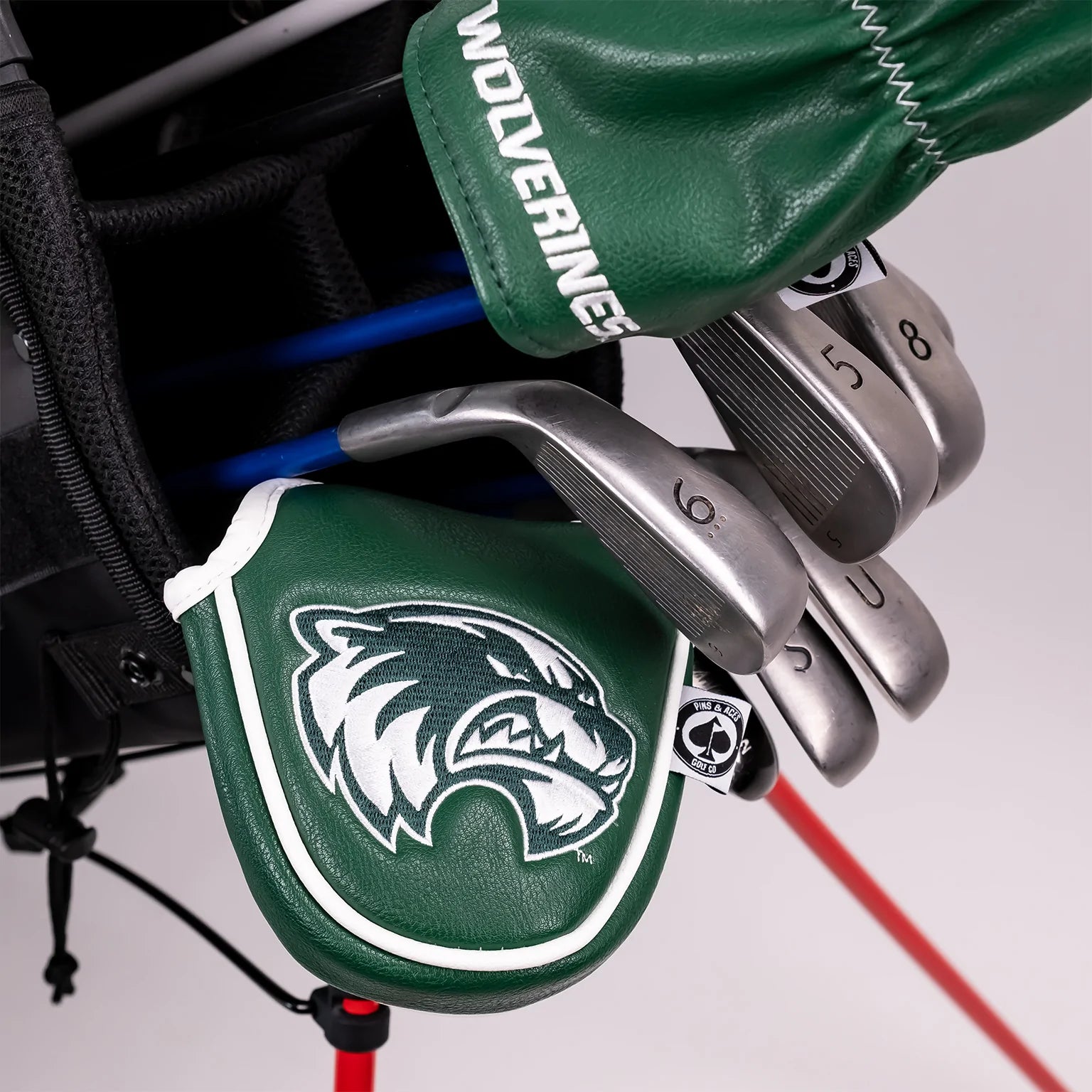 Utah Valley University mallet putter cover in green with a white logo, positioned among golf clubs in a bag.